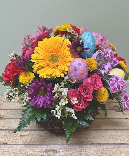 Egg-cited ES30 - Bright and cheery like a basket of dyed eggs, this spring arrangement will make any recipient feel truly egg-cited!  This nest style basket will arrive with Gerber daisies, carnations, and spray roses and finished with a cheerful bow and assorted eggs.  