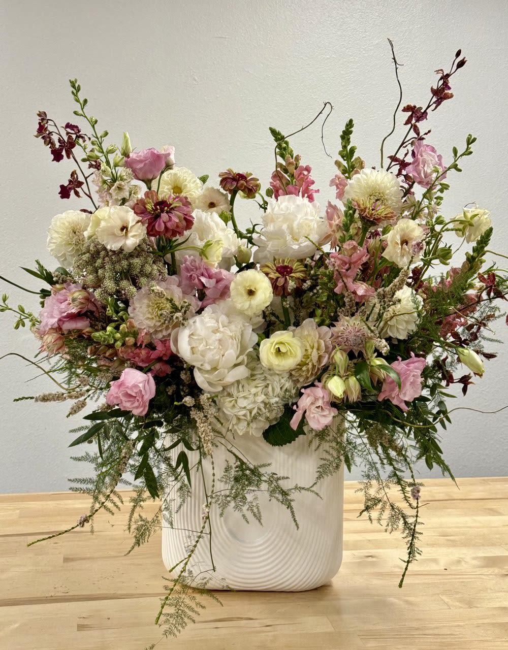 Large airy arrangement of white and pink flowers with burgundy accents in a tall white ceramic vase.