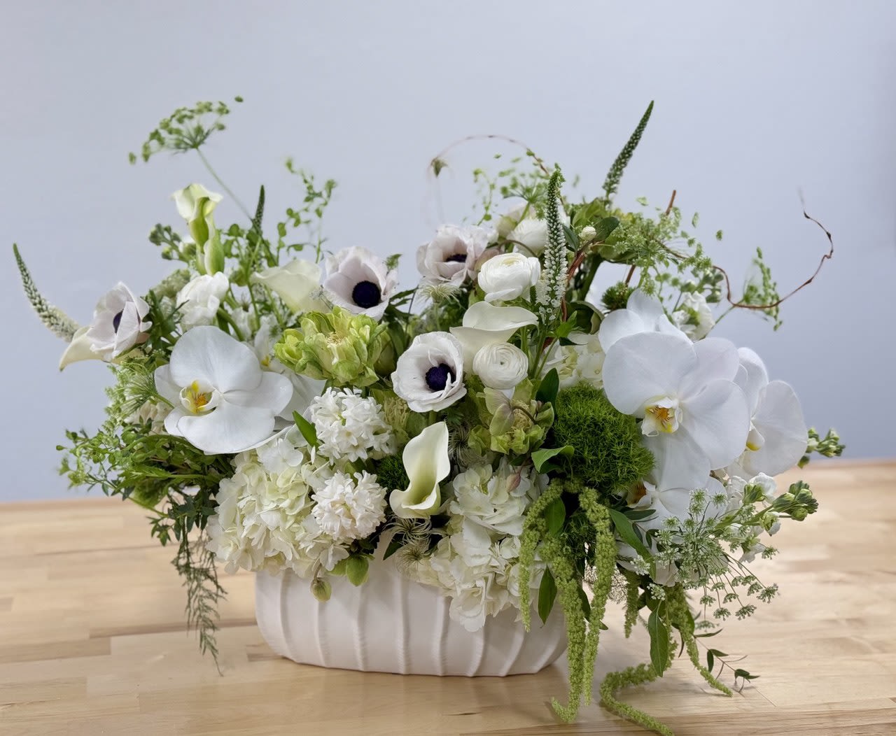 Low white arrangement with orchids, anemones, calla lilies, and hydrangeas in a white ceramic vase