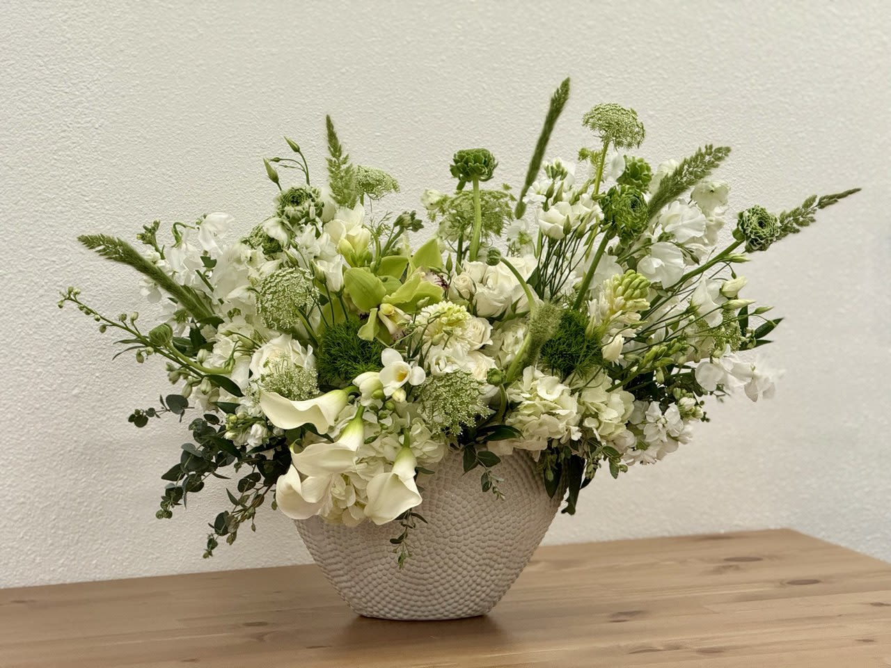 White and green flower arrangement in a textured white bowl on a wooden surface