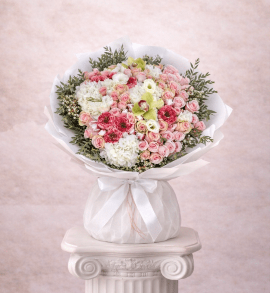 Large round bouquet of pink spray roses and white hydrangeas wrapped in white paper and ribbon
