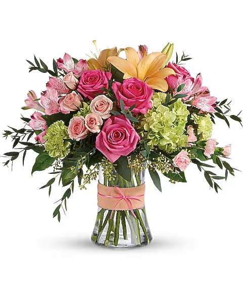 Blush Life Bouquet - Go ahead, make them blush! This luxurious bouquet of roses, lilies and hydrangea in fresh shades of pink, peach and green is sure to put some cheerful color in their cheeks! The delicate ribbons dress up the graceful keepsake vase. This sweet arrangement features green hydrangea, hot pink roses, pink spray roses, peach asiatic lilies, pink alstroemeria, green carnations, pink miniature carnations, seeded eucalyptus, parvifolia eucalyptus, and lemon leaf. Delivered in a glass gathering vase.