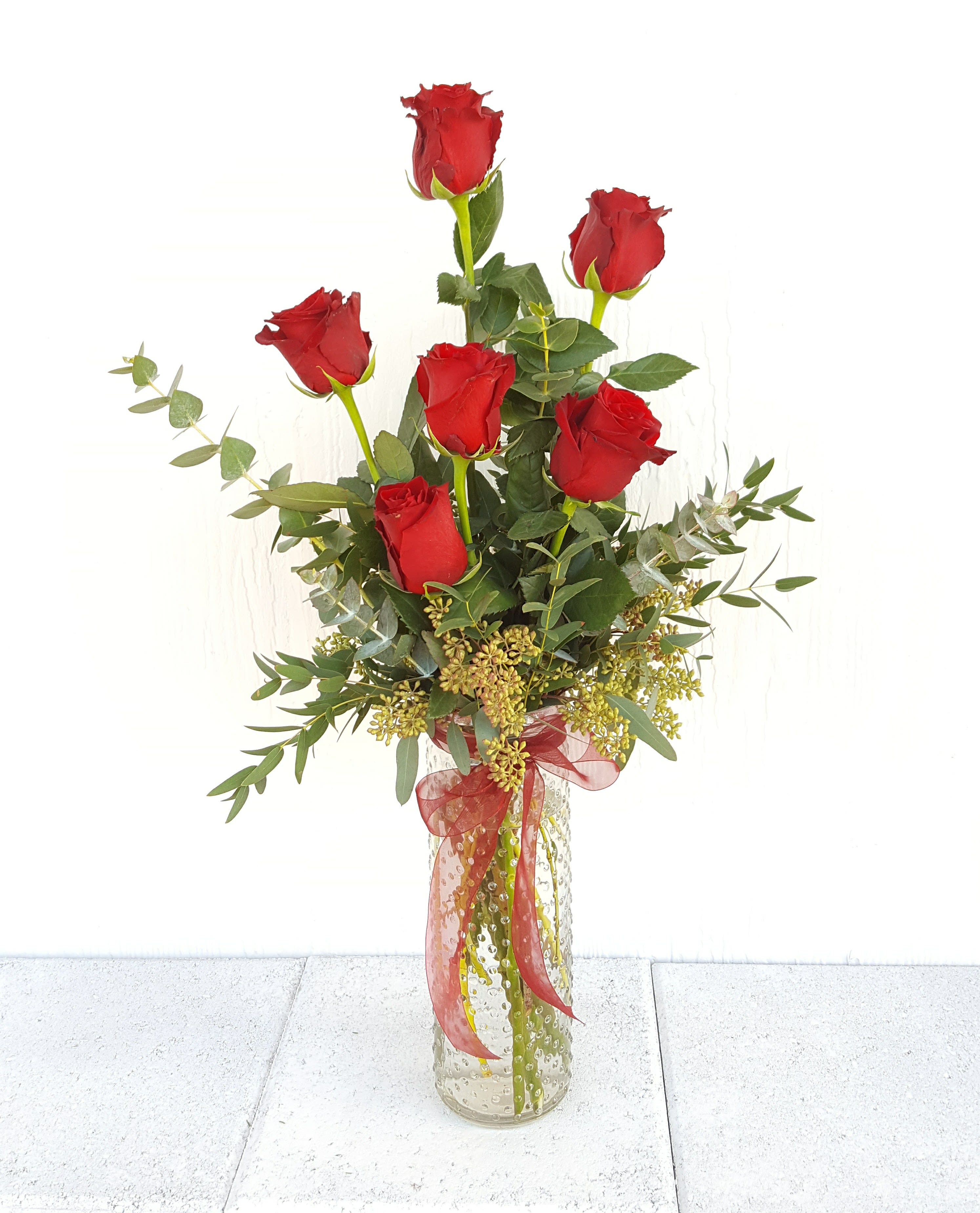 Tall bouquet of red roses in a clear glass vase with ribbon