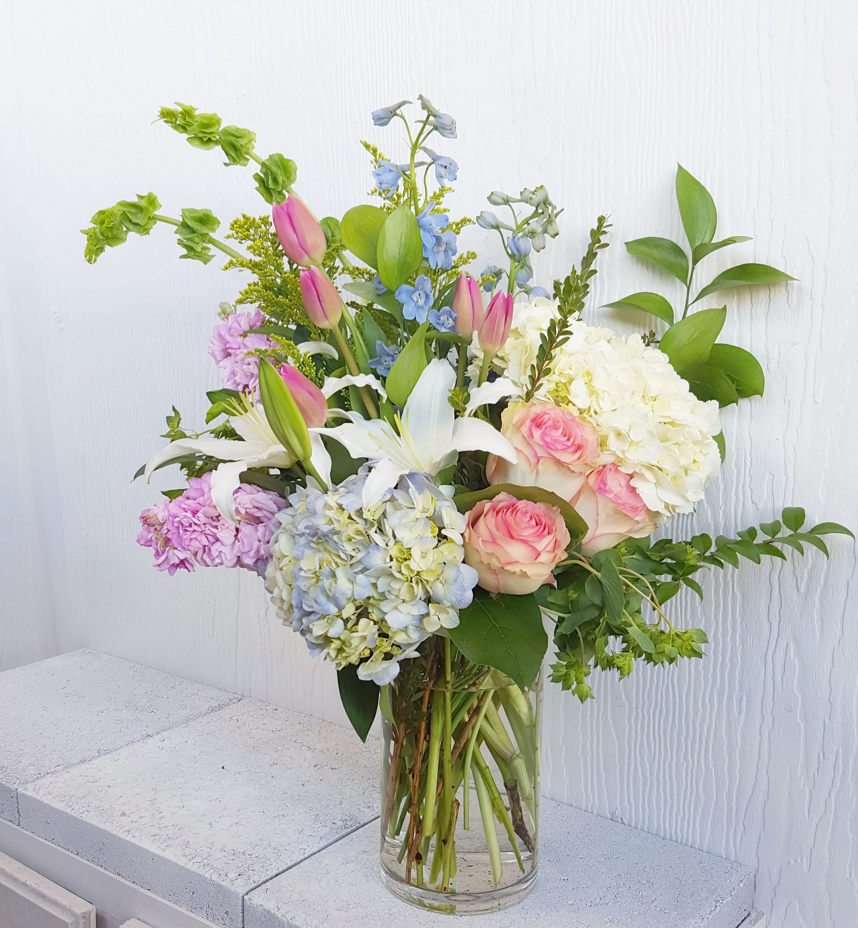 Springtime arrangement  - Blush pinks and soft blues welcome the spring season.   Approx 25" tall. Upgrades go in same vase for a fuller look, premium is in a bigger vase and more Flowers. 