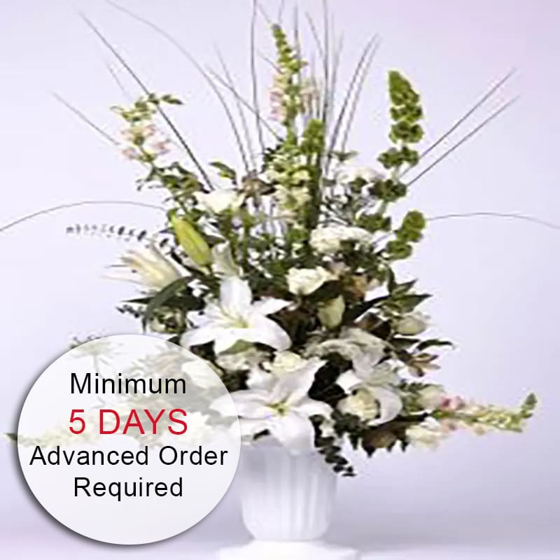 Tall white floral arrangement with lilies and snapdragons in a white urn-style vase