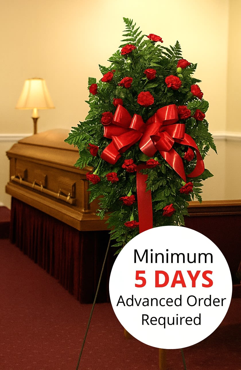 Tall funeral spray of red carnations with large red bow on an easel beside a casket.