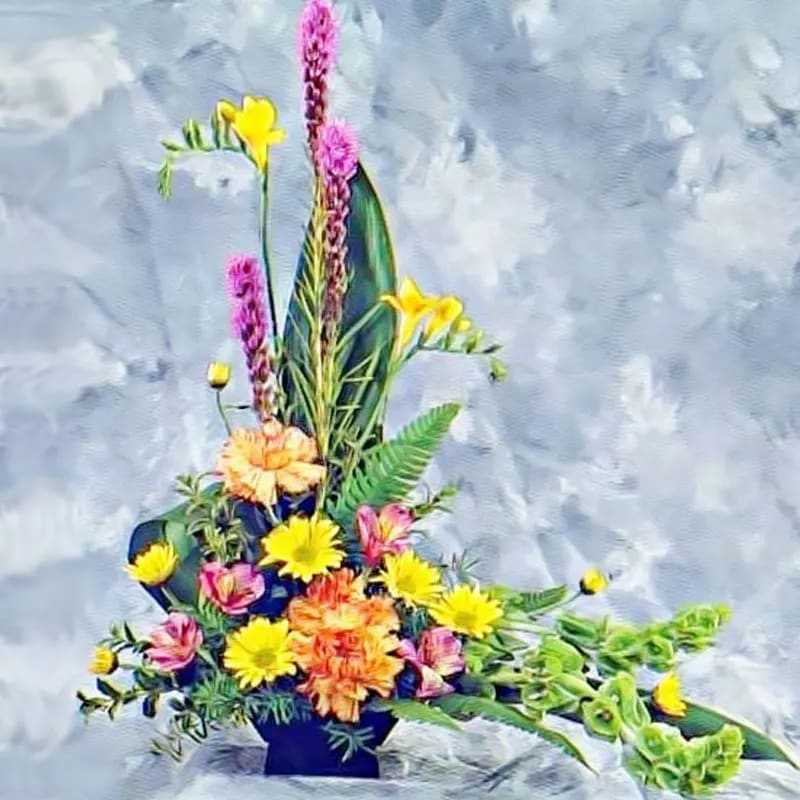 Tall asymmetrical arrangement with yellow, orange, pink, and purple flowers in a black container