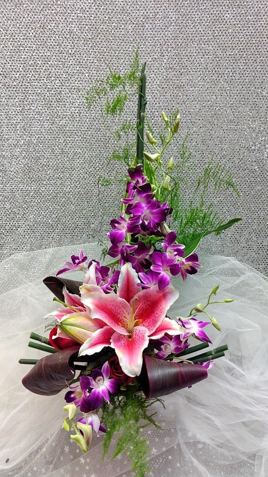 Asymmetrical pink lily and purple orchid arrangement with tall linear accents on sheer fabric