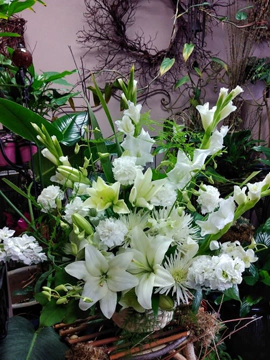 Tall all-white floral arrangement with lilies, carnations, and other blooms in a ceramic container