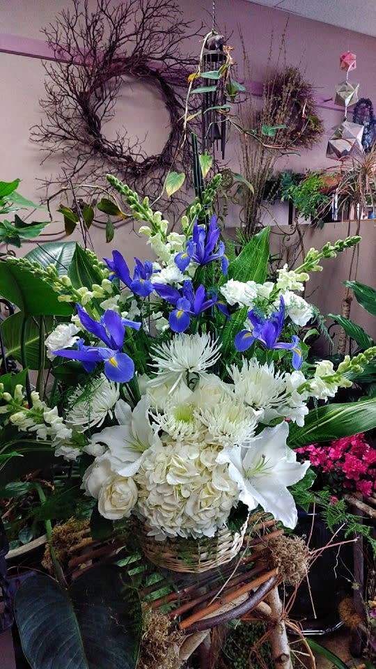 Tall arrangement of blue irises and white lilies, hydrangeas, and mums in a woven basket