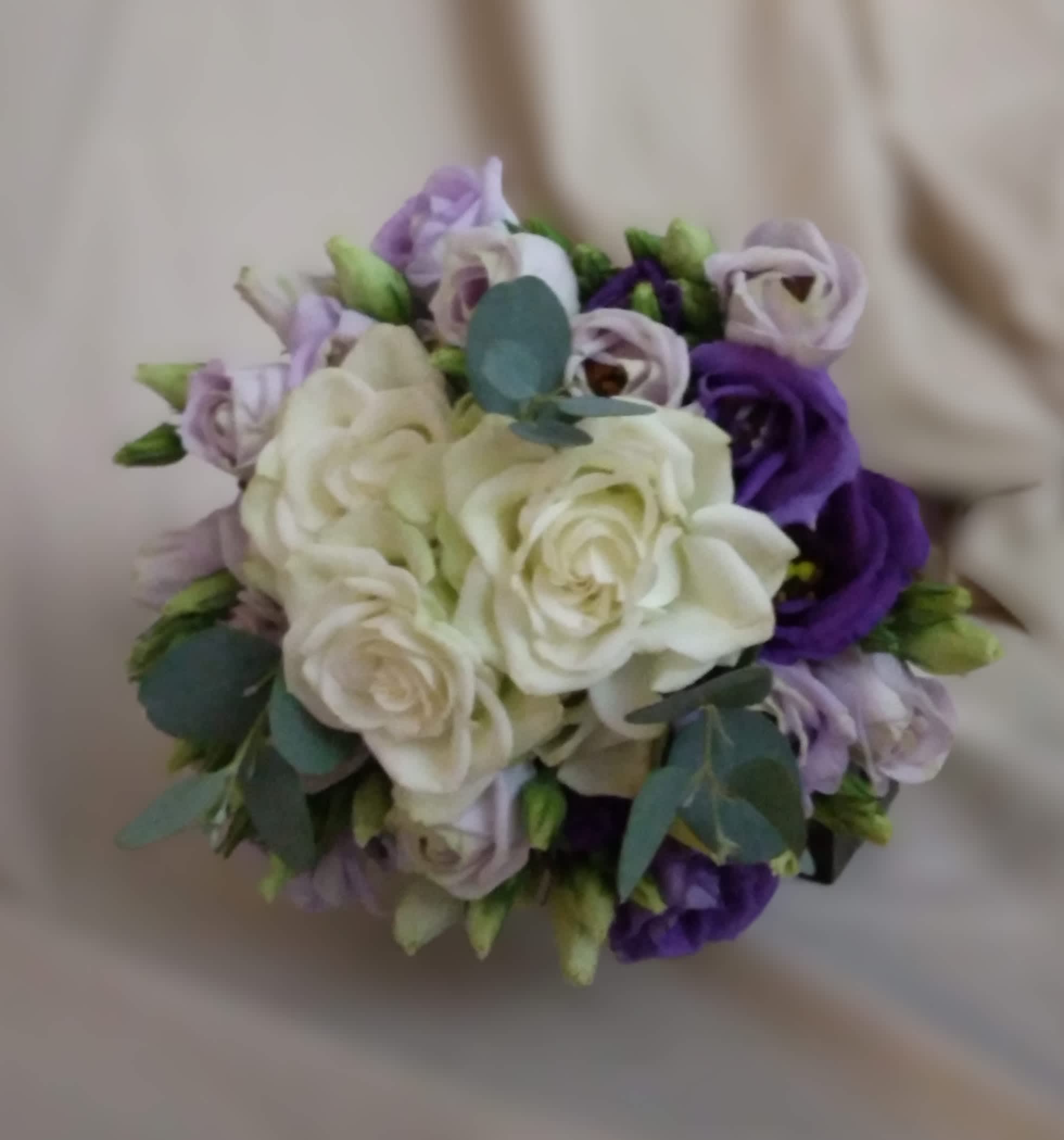 Round bouquet of white roses with purple and lavender lisianthus on a neutral background