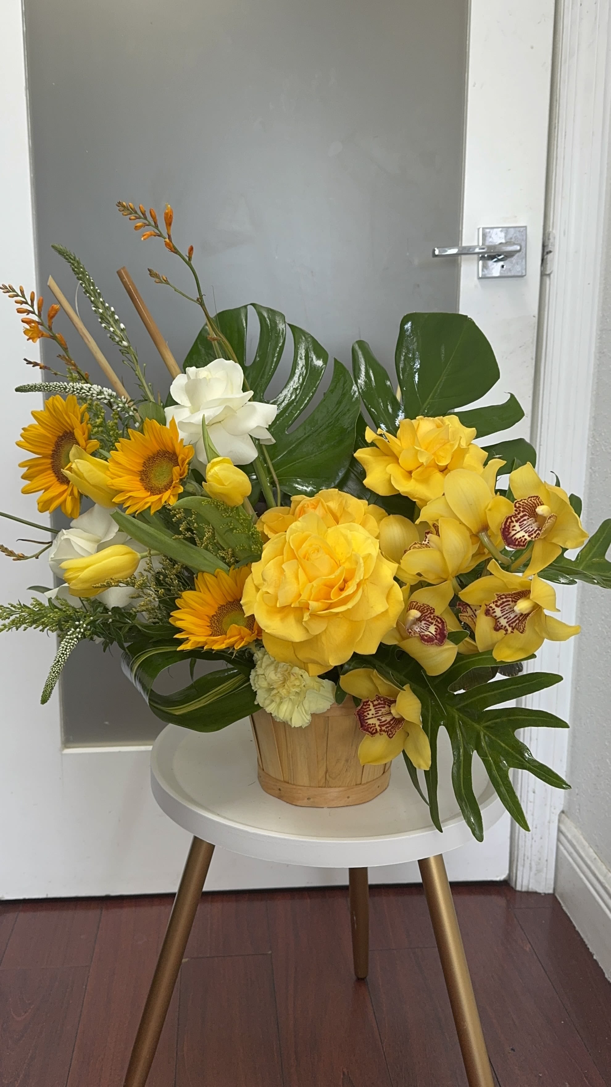 Yellow floral arrangement in a wooden basket with orchids and sunflowers