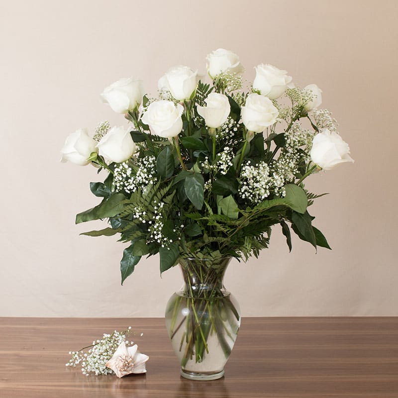 Tall arrangement of white roses and baby's breath in a clear glass vase on a wooden table