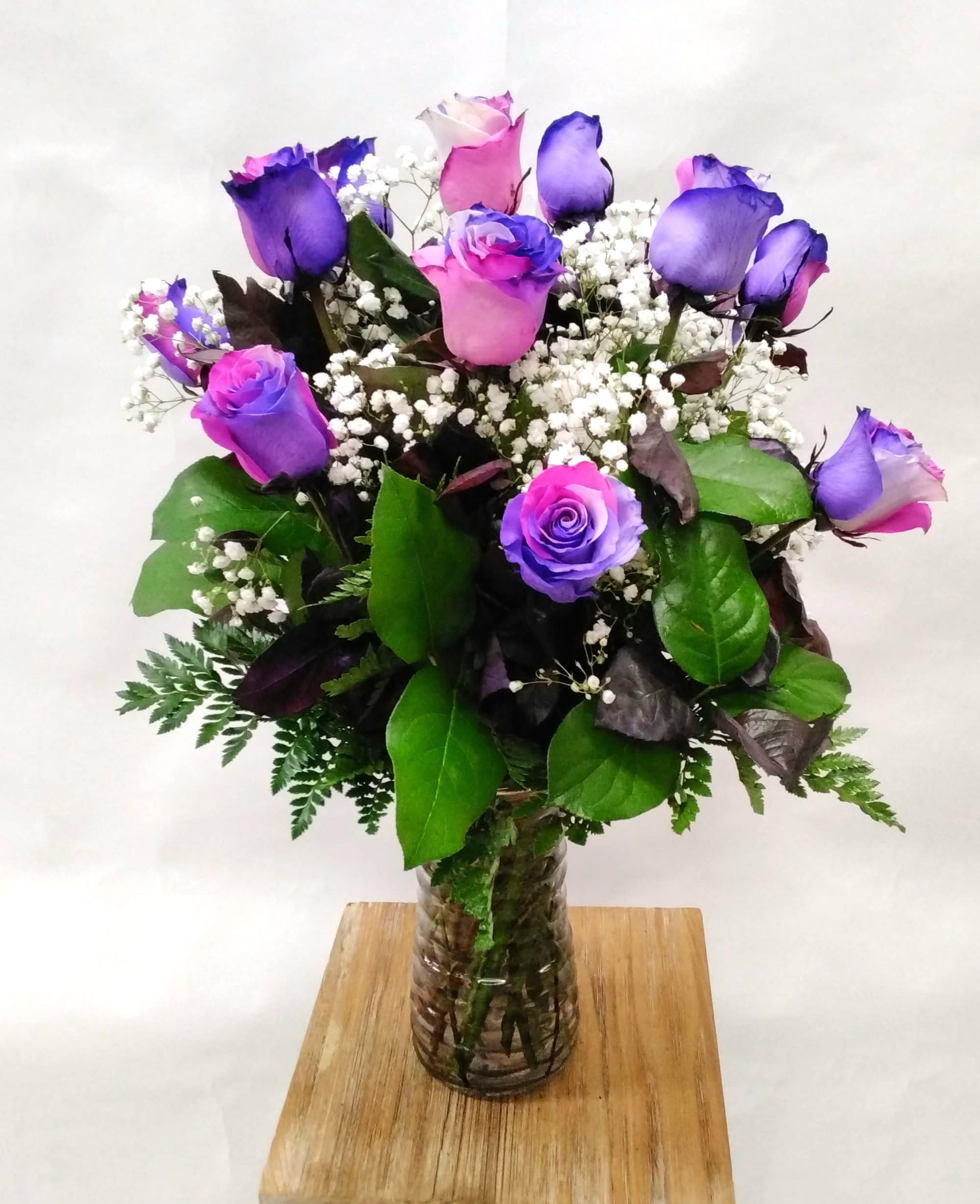 Tall bouquet of pink and purple roses with white filler flowers in a clear glass vase