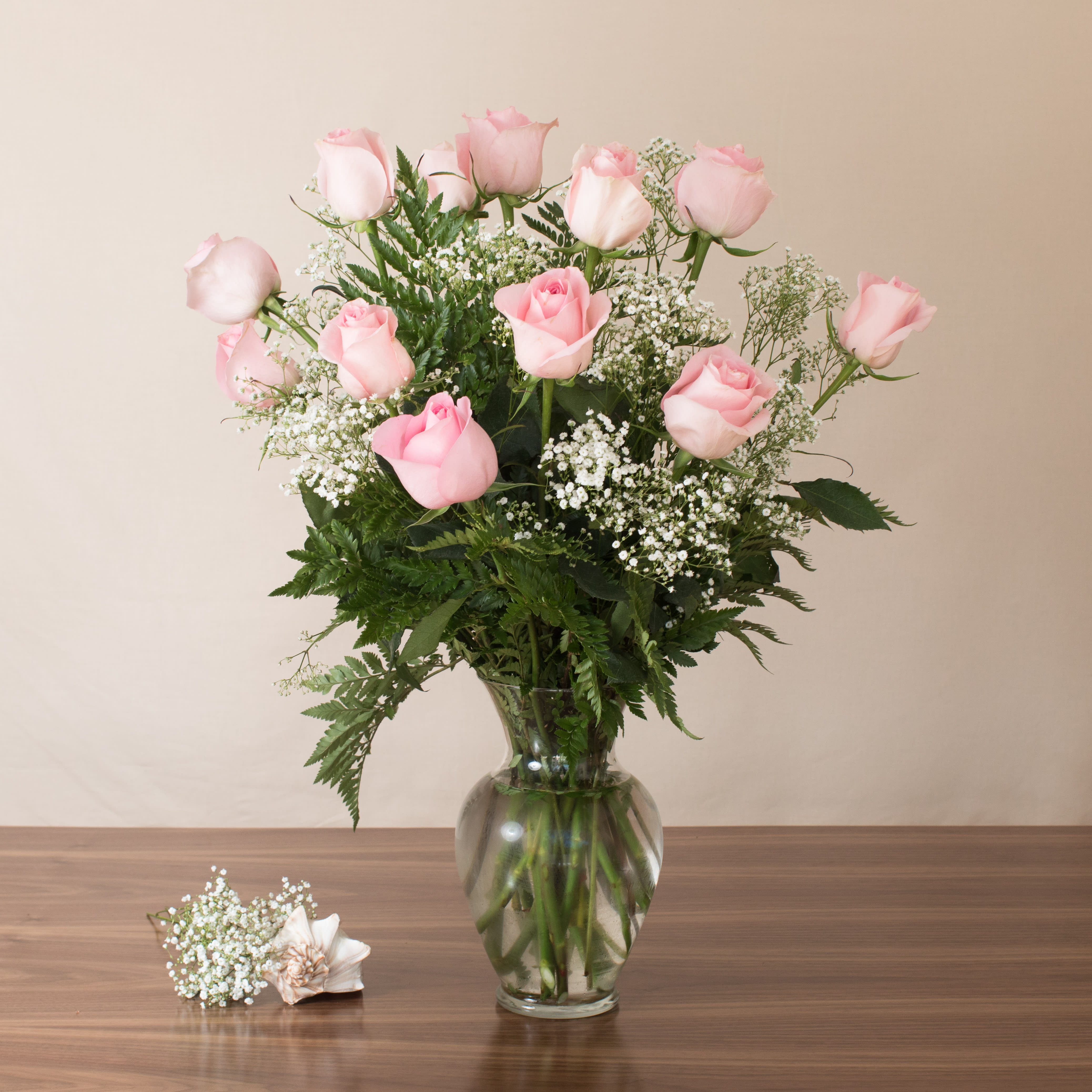 Tall bouquet of light pink roses and white filler flowers in a clear glass vase