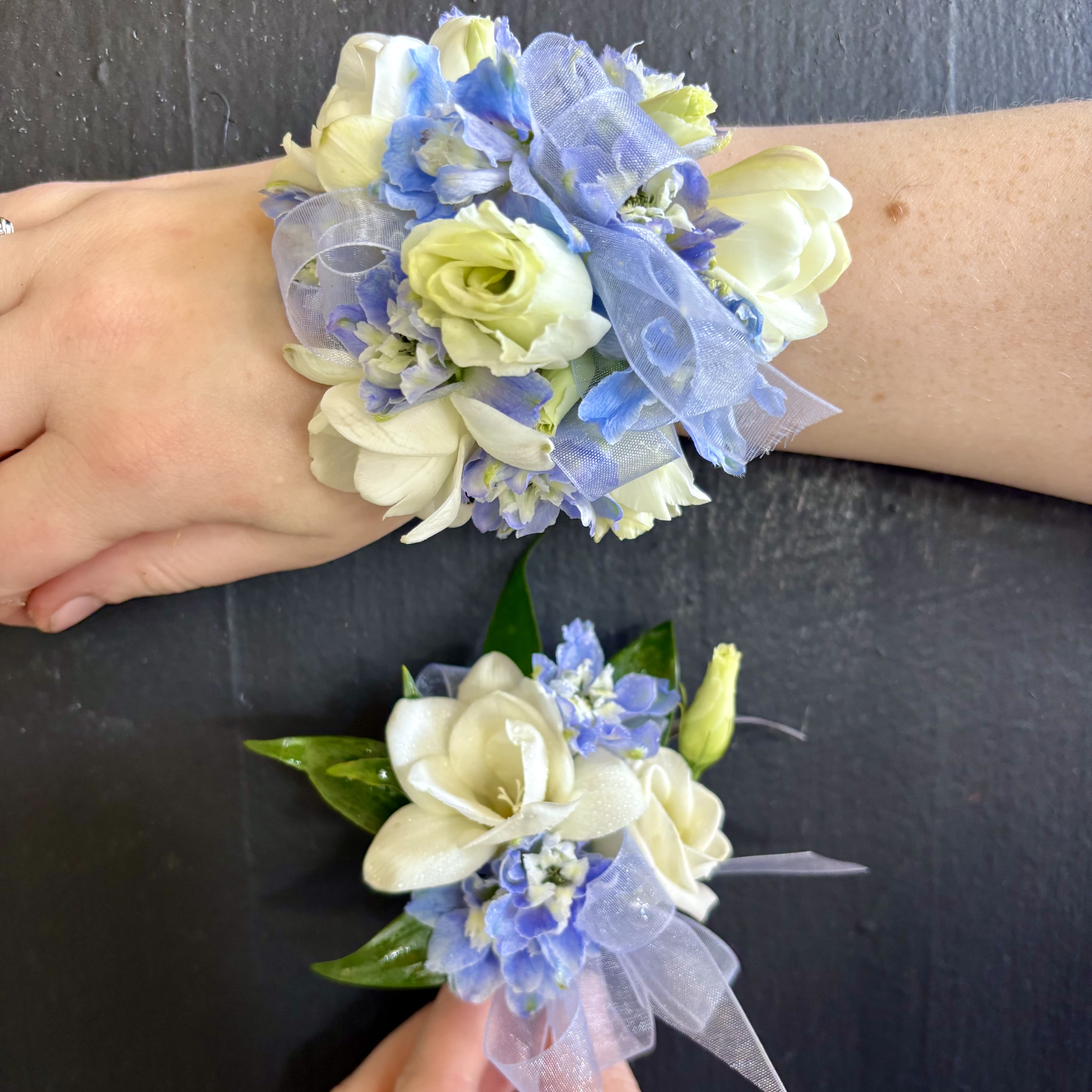 Blue and White Corsage/ Boutonniere Set - A Corsage and Boutonniere set in Blue and White. Topped off with a silky blue ribbon. Our corsages are made with either a silver or gold band.Please let us know in the special instructions section if you would like any substitutions. We will do our best to satisfy your requests. Colors can be substituted only when flowers are available.  