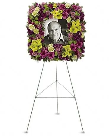 Square memorial floral frame of purple and green blooms on a stand with a photo in the center