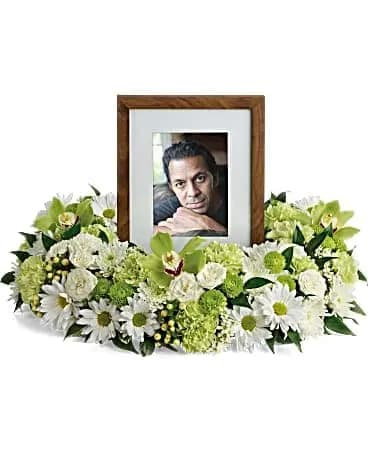 Low white and green floral ring encircling a wooden photo frame with a portrait