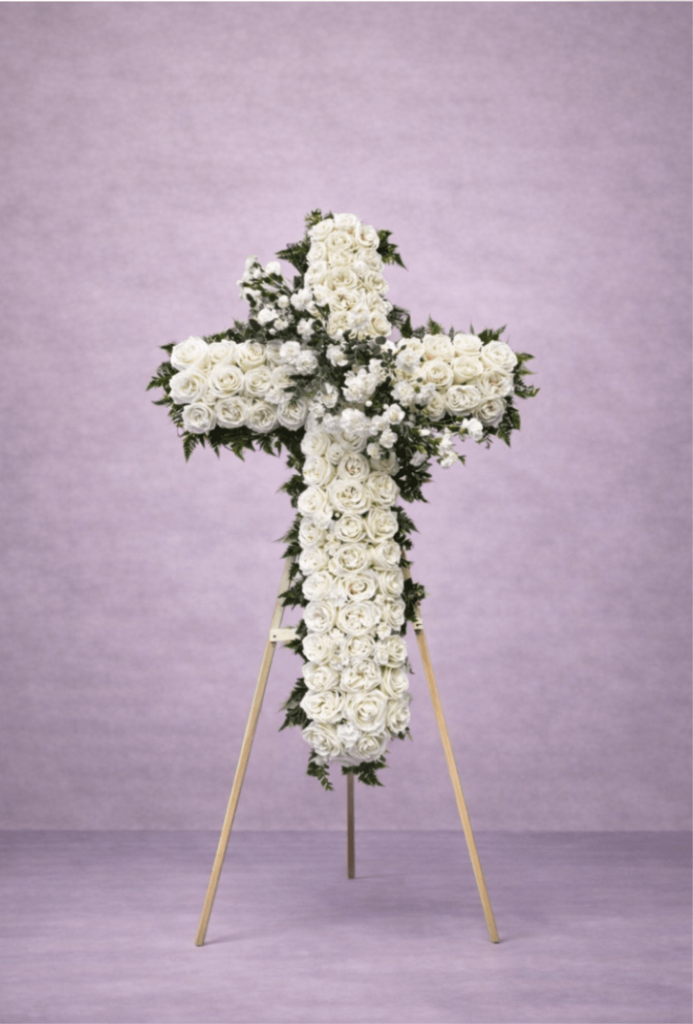 Standing cross-shaped spray of white roses on a wooden easel against a soft lavender background