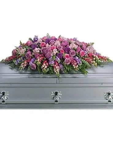 Lavender Tribute Casket Spray - Like a heartfelt embrace, this beautiful casket spray delivers comfort and love in an extraordinary way. A wonderful array of lavender and pink flowers with just the right amount of greenery is a lovely way to pay tribute to someone who will always be with you in heart, mind and spirit. Lovely lavender and pink roses, snapdragons, alstroemeria, chrysanthemums, fern, eucalyptus and more create this tribute that is overflowing with grace and love. 