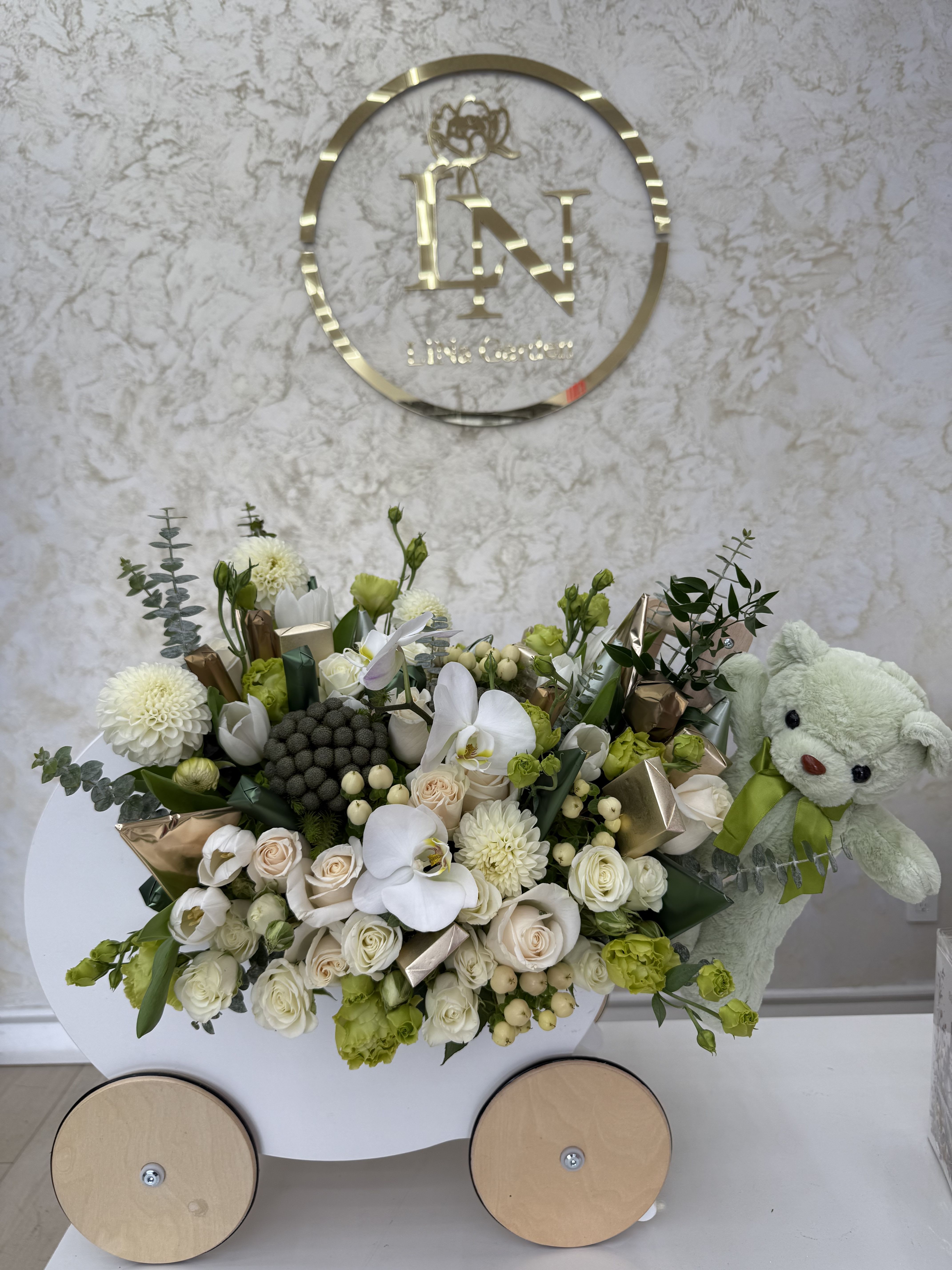 White and green floral arrangement with a teddy bear in a cart