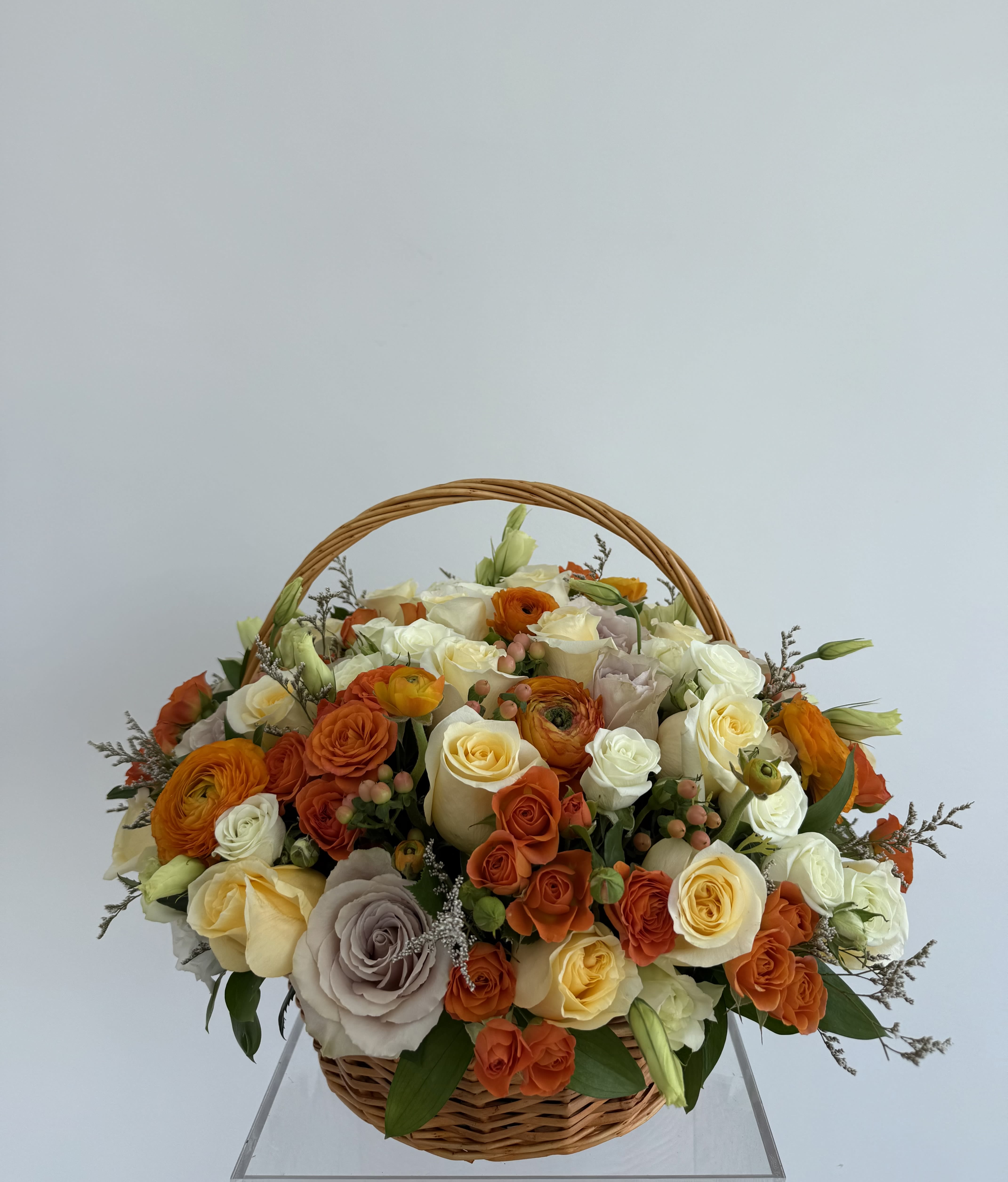Basket of orange, cream, and white roses with ranunculus