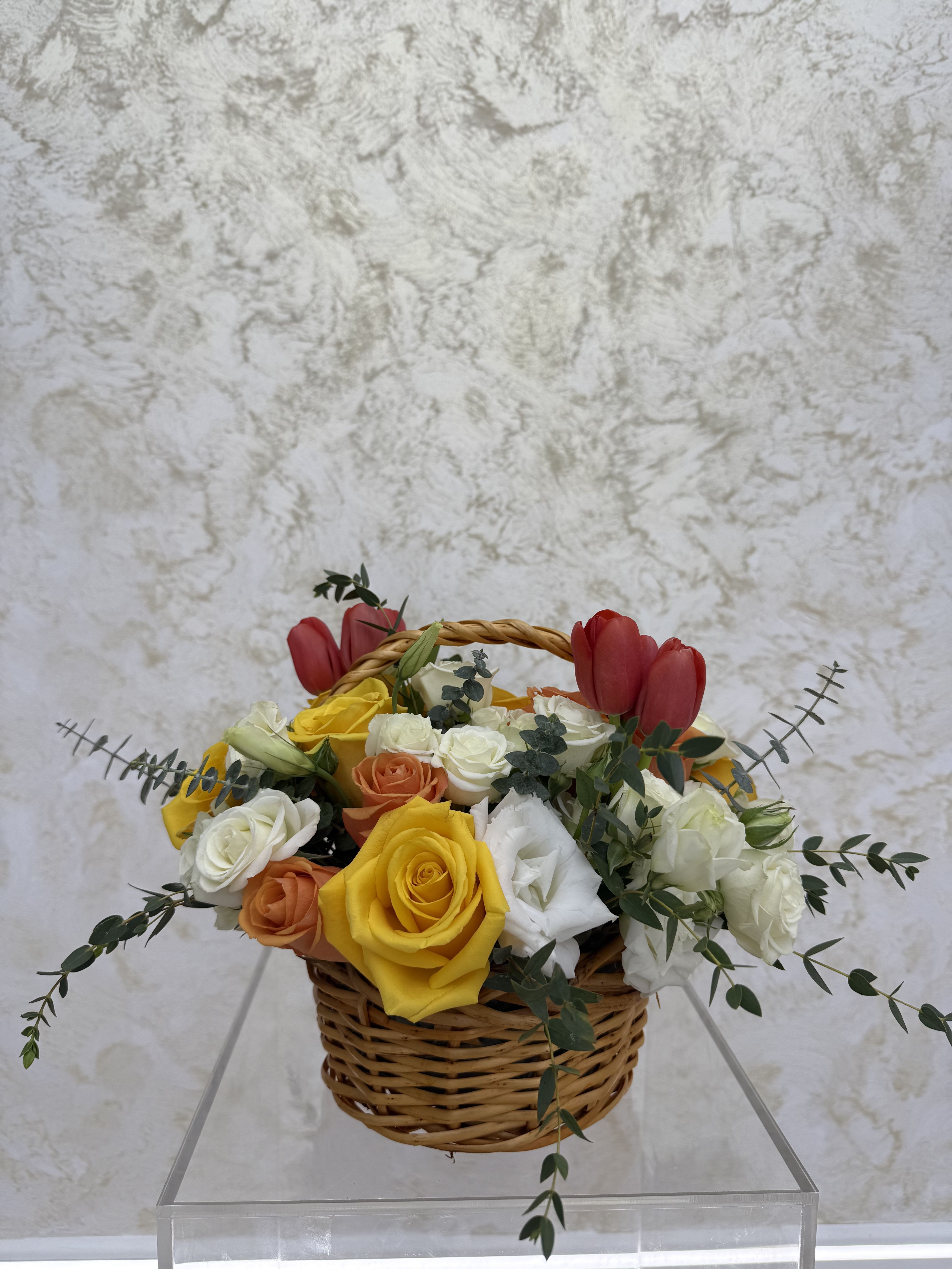 Basket of mixed roses with red tulips and greenery