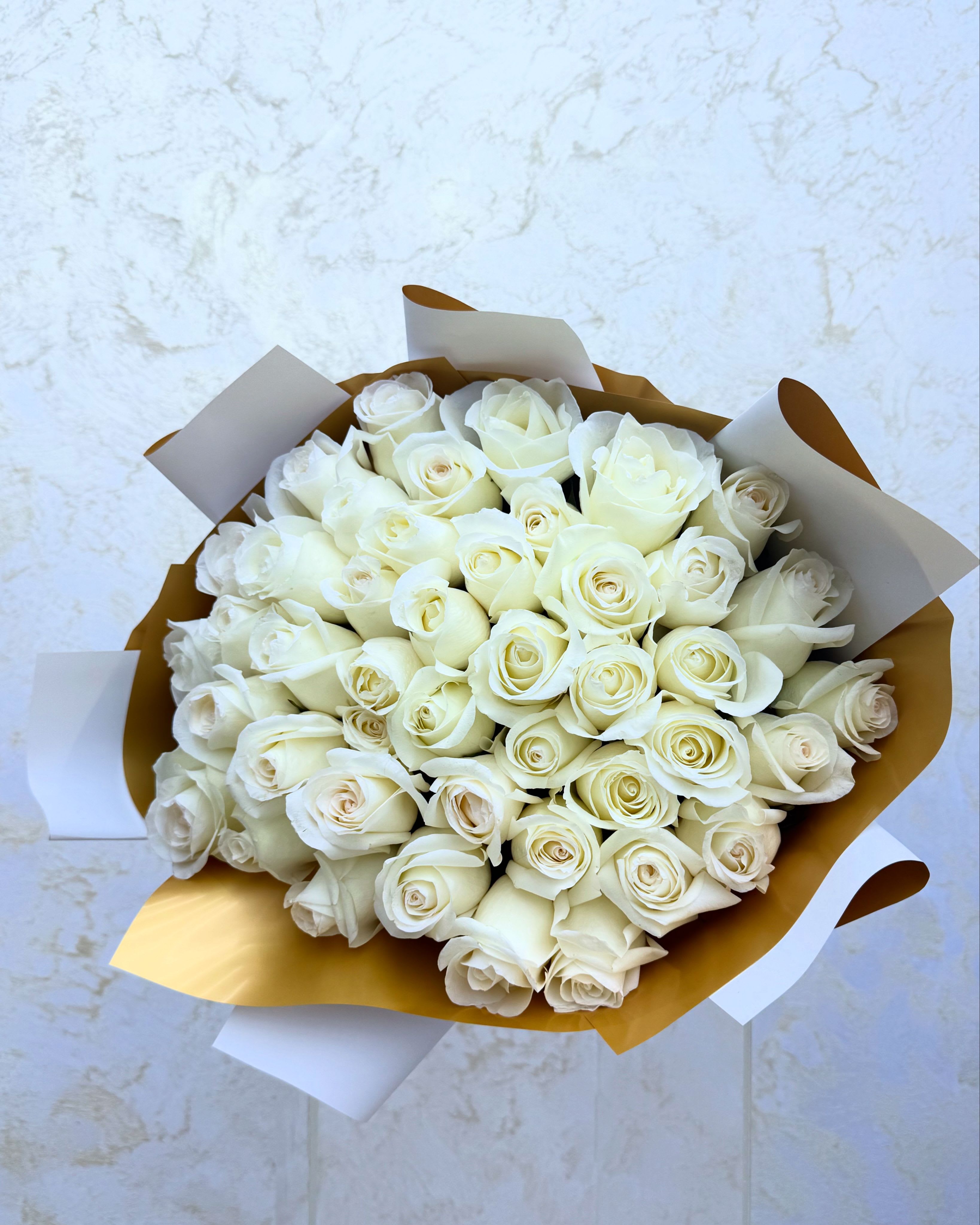Bouquet of white roses wrapped in gold and white paper