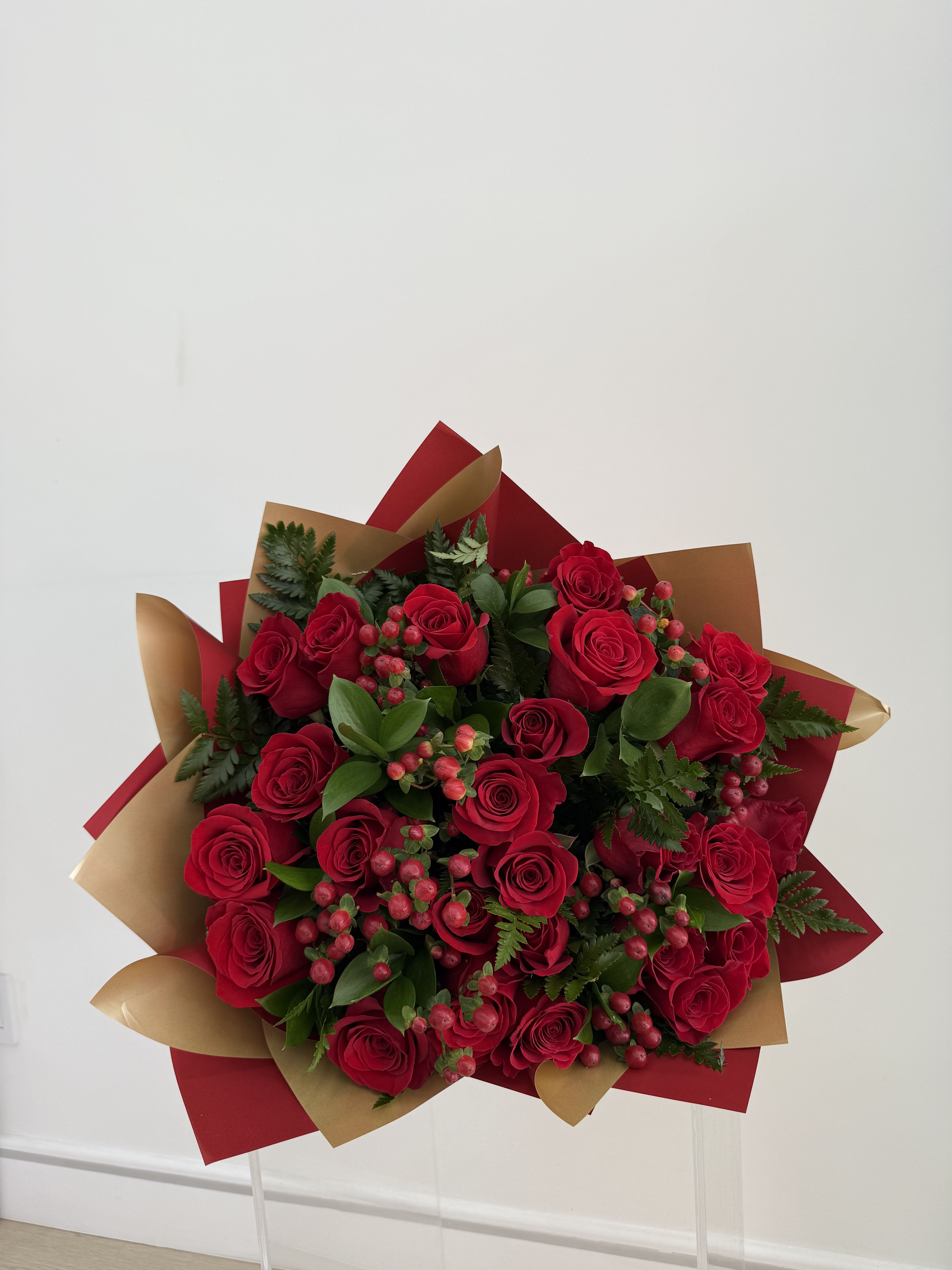 Bouquet of red roses with berries and greenery in red and gold wrap