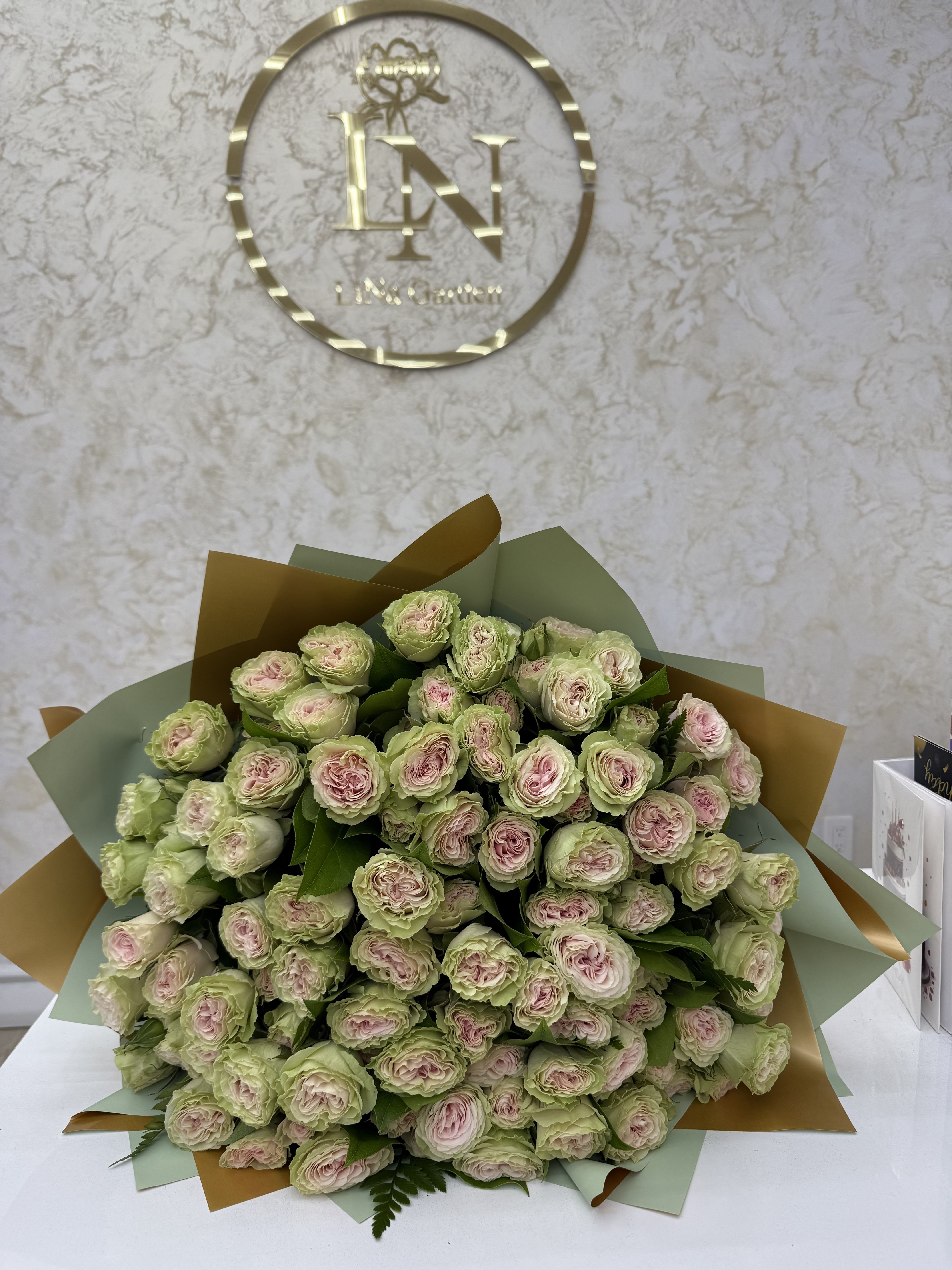 Large bouquet of pale pink and green roses wrapped in pastel paper
