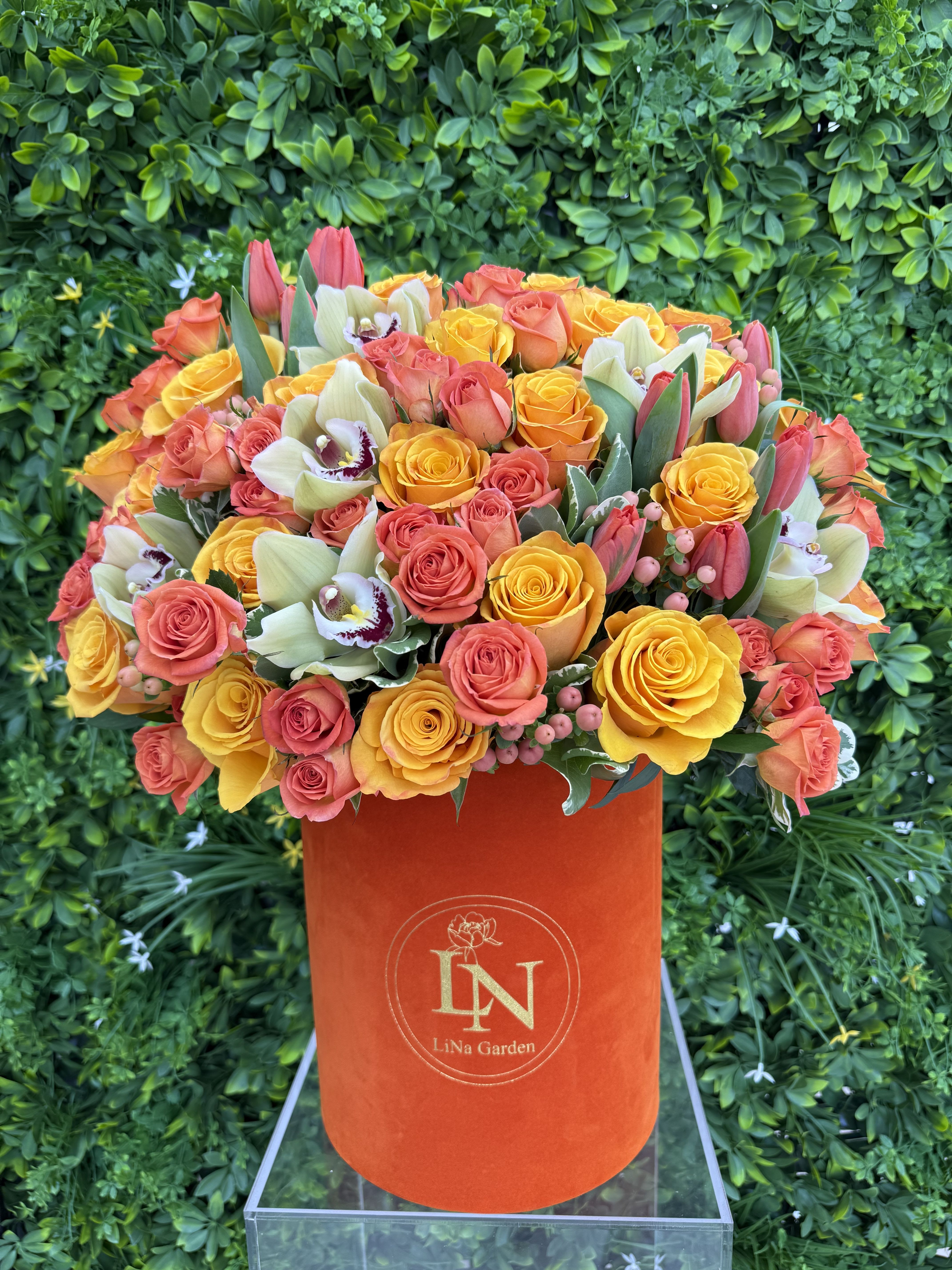 Orange hatbox arrangement of yellow and coral roses with orchids