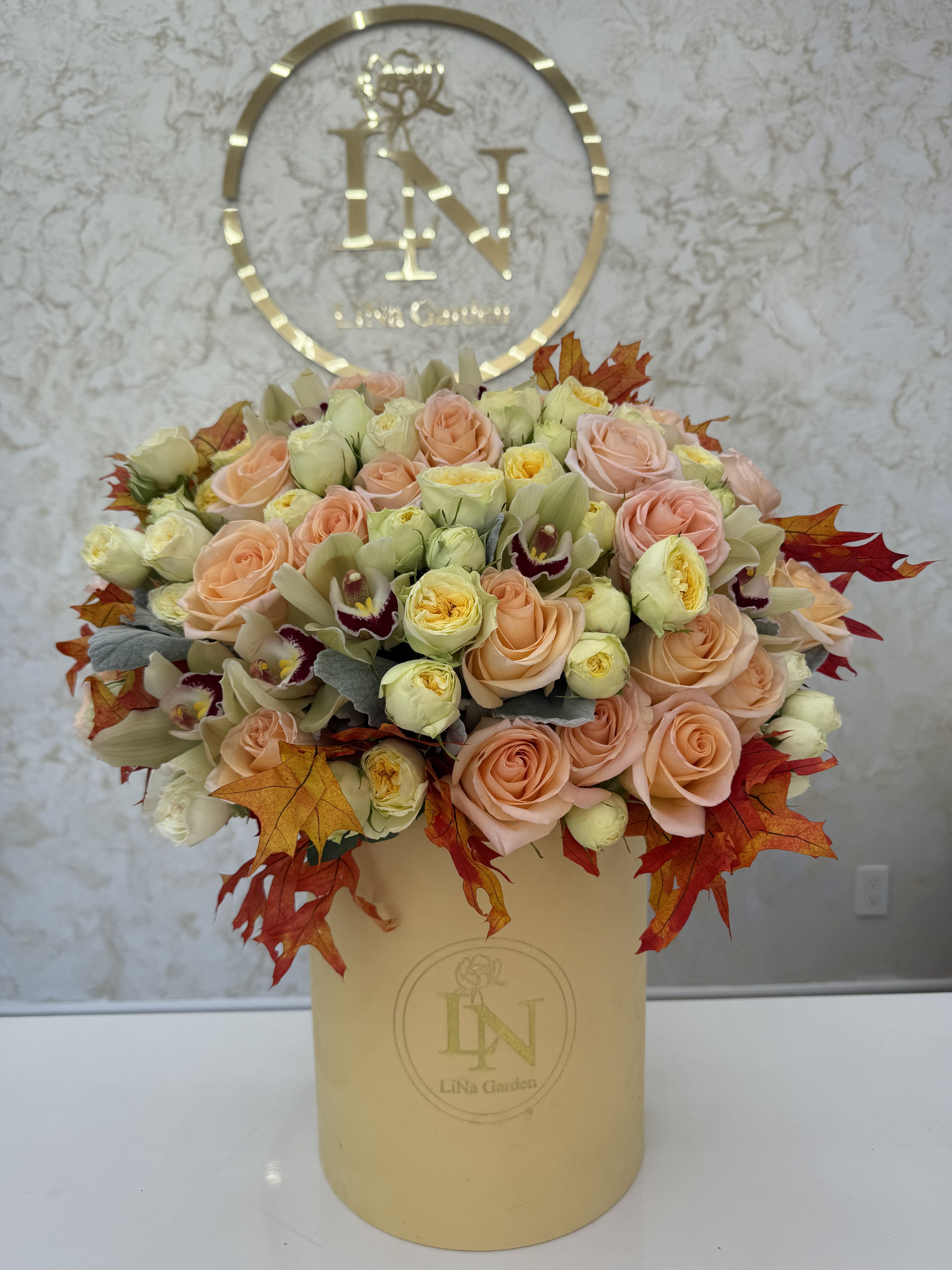 Peach roses and cream blooms arranged in a beige hatbox with autumn leaves