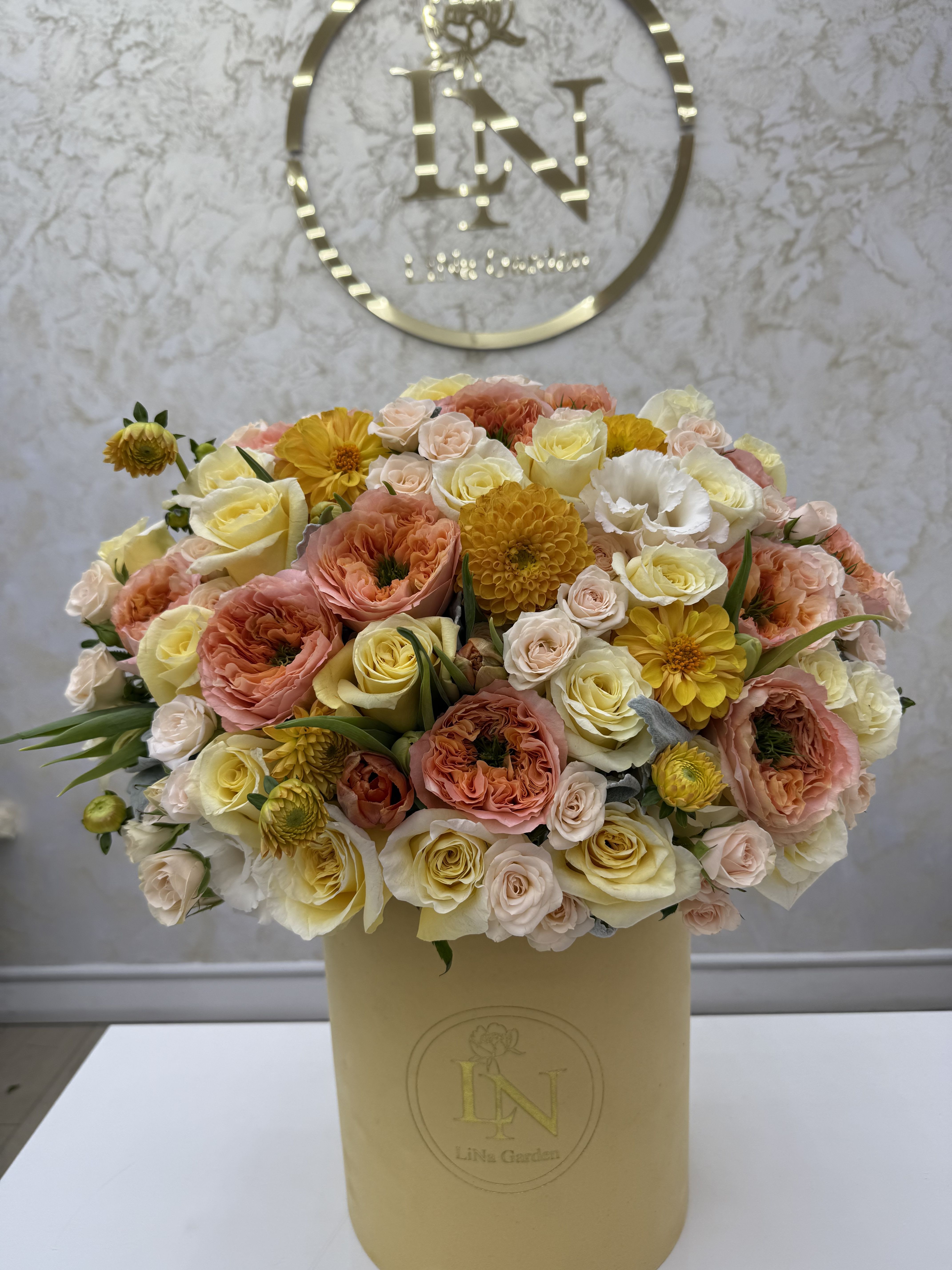 Mixed bouquet of peach, cream, and yellow flowers in a beige hatbox