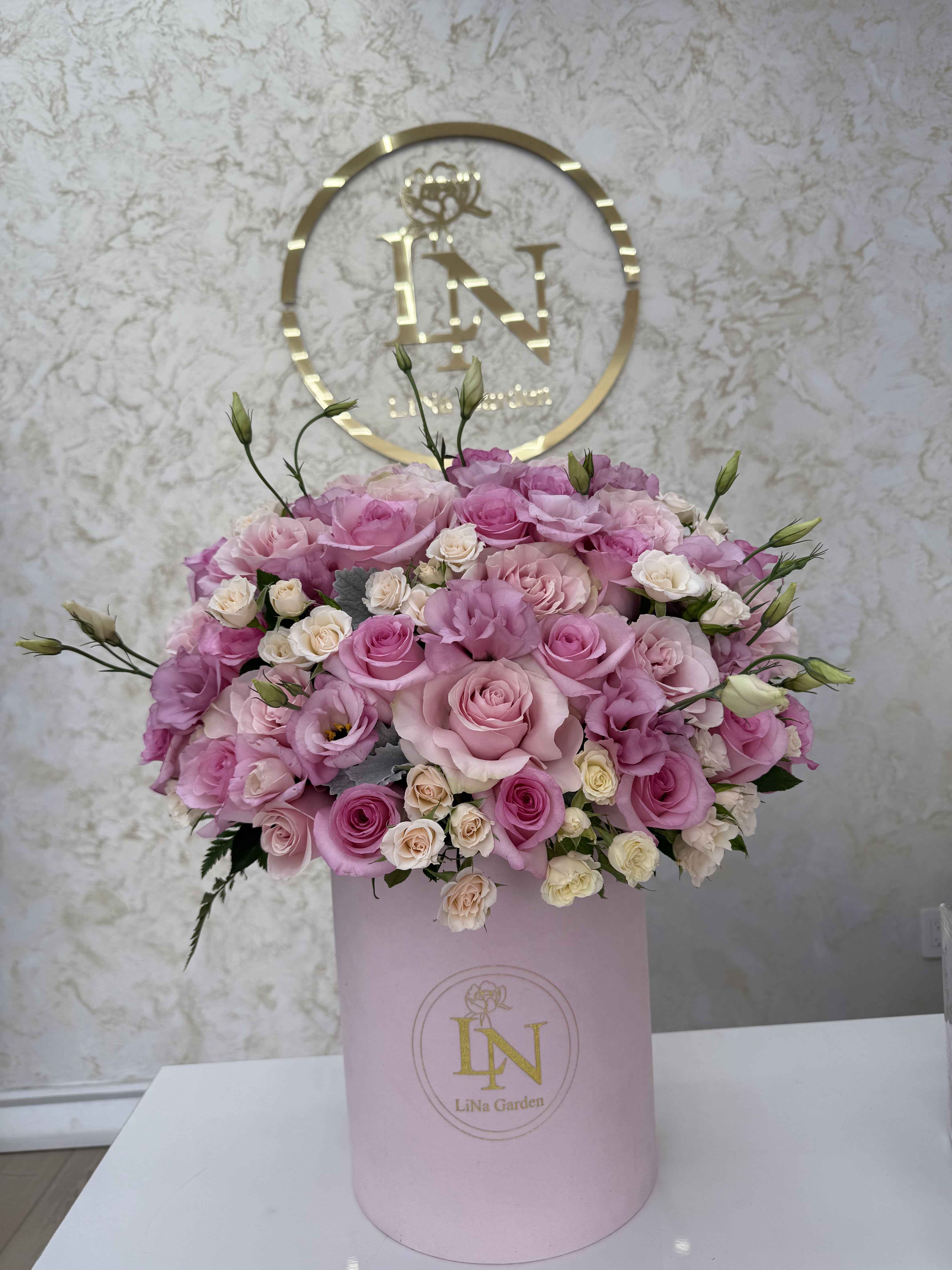 Pink and cream roses arranged in a round pink box