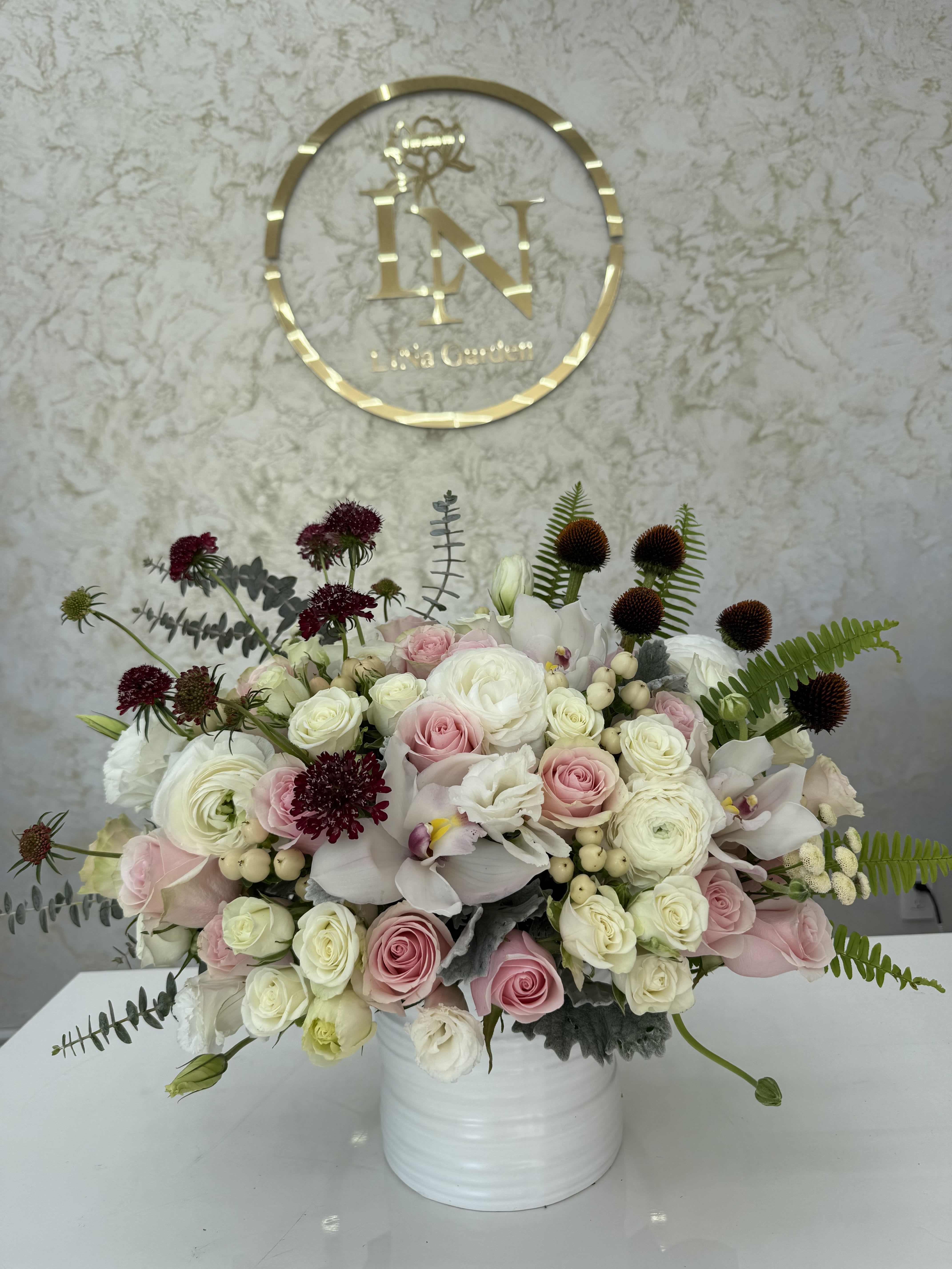Pink and white rose arrangement in a white vase with dark accent blooms