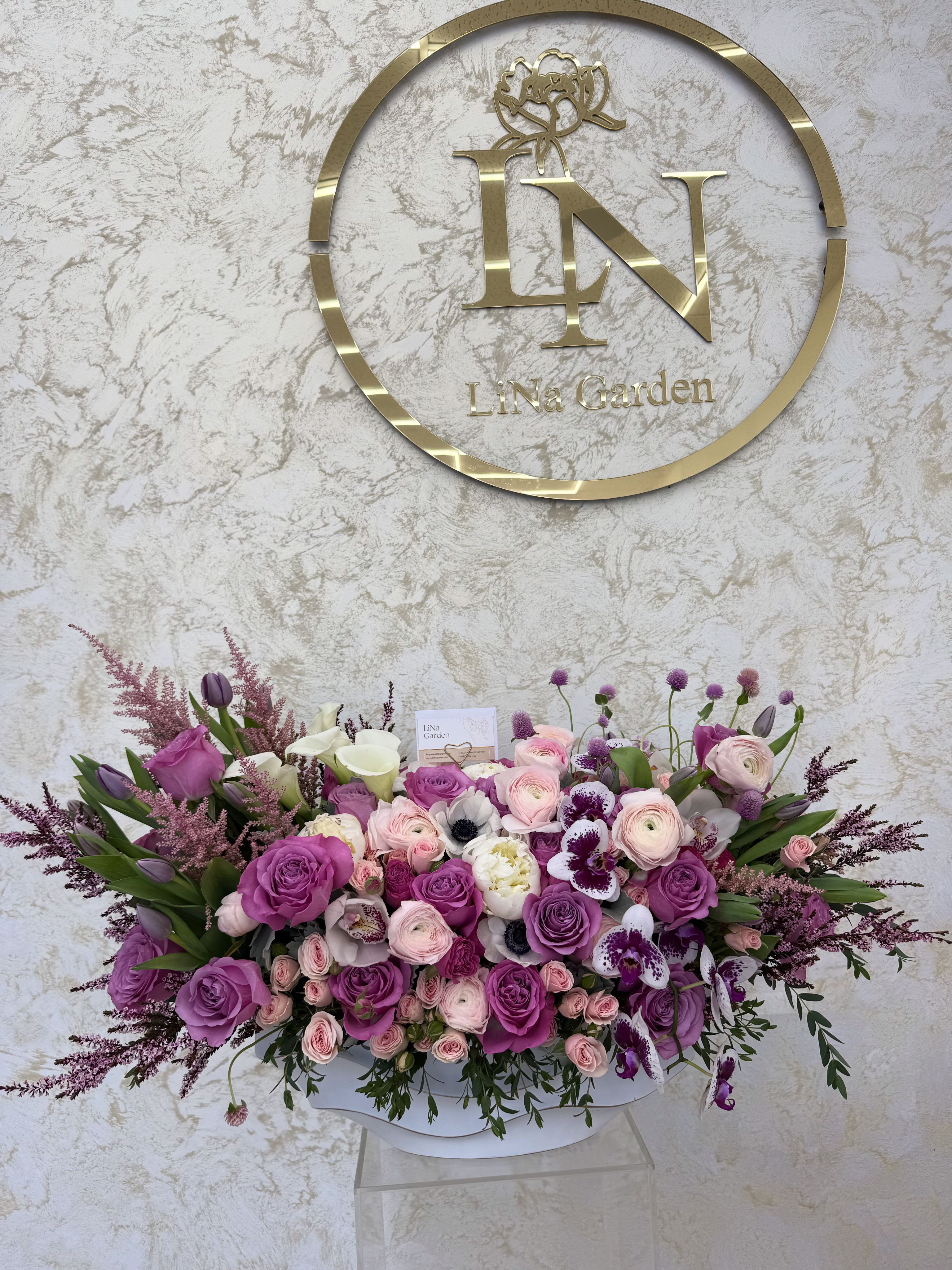 Large bouquet of purple and pink roses with white orchids in a white container
