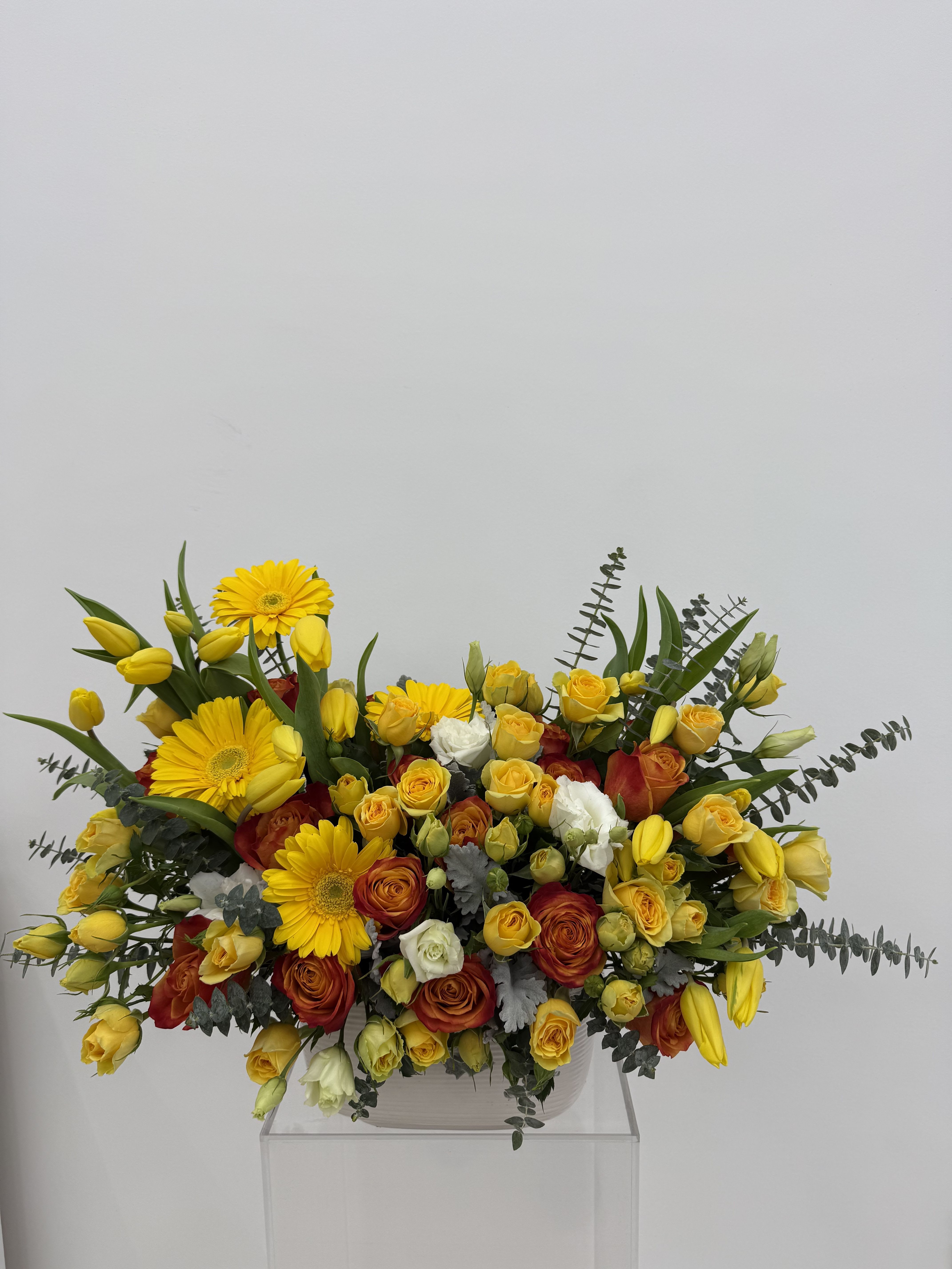Yellow gerberas and roses arranged in a low white container