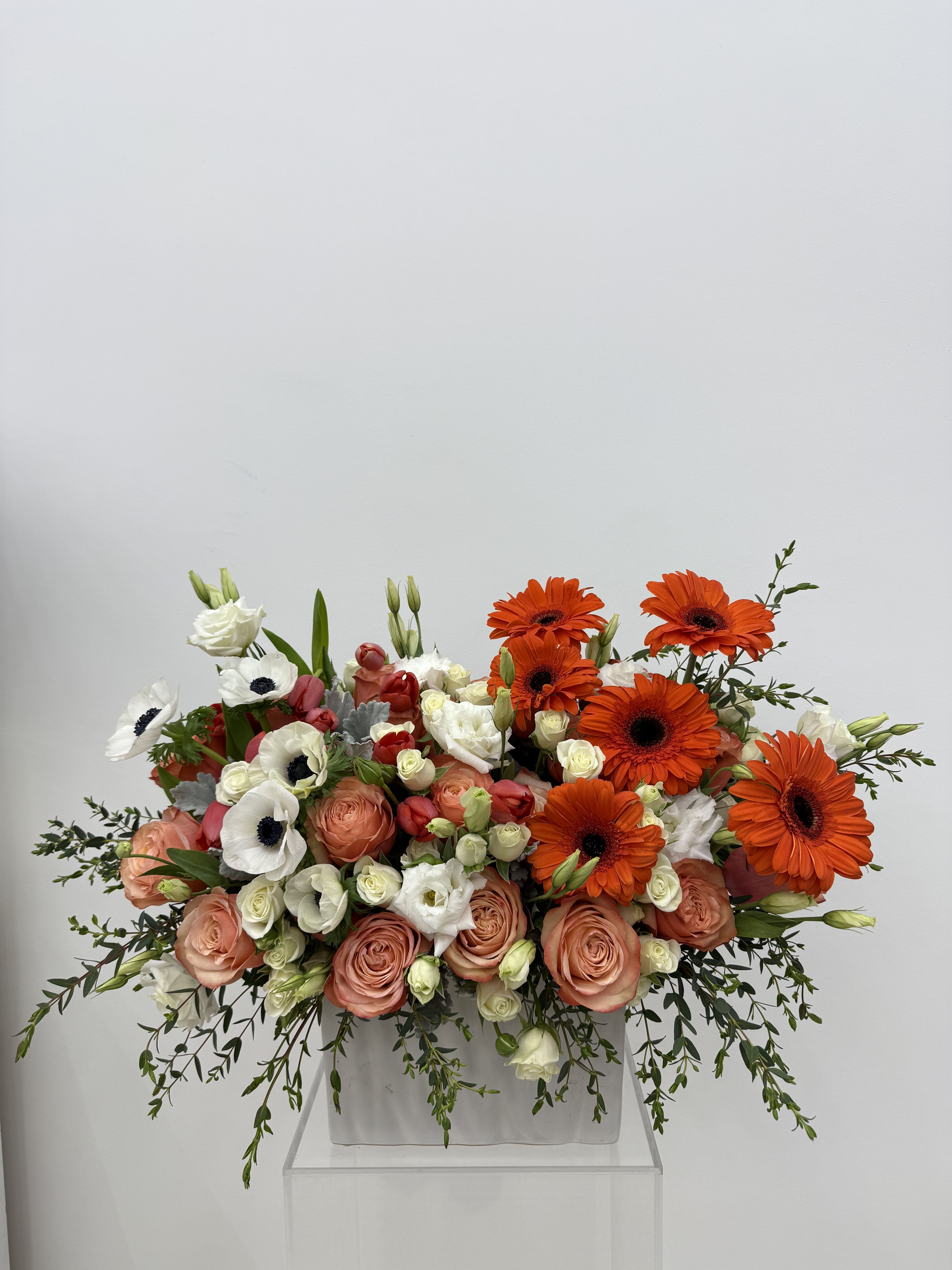 Large bouquet of orange gerbera daisies and peach roses in a white container