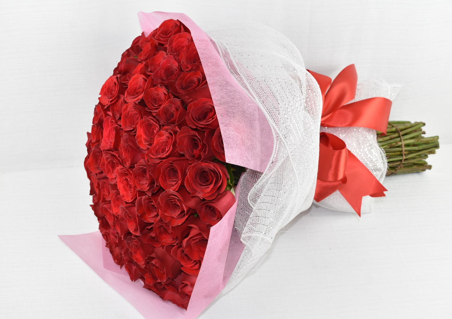 Large bouquet of red roses wrapped in pink paper and white mesh with a red satin bow