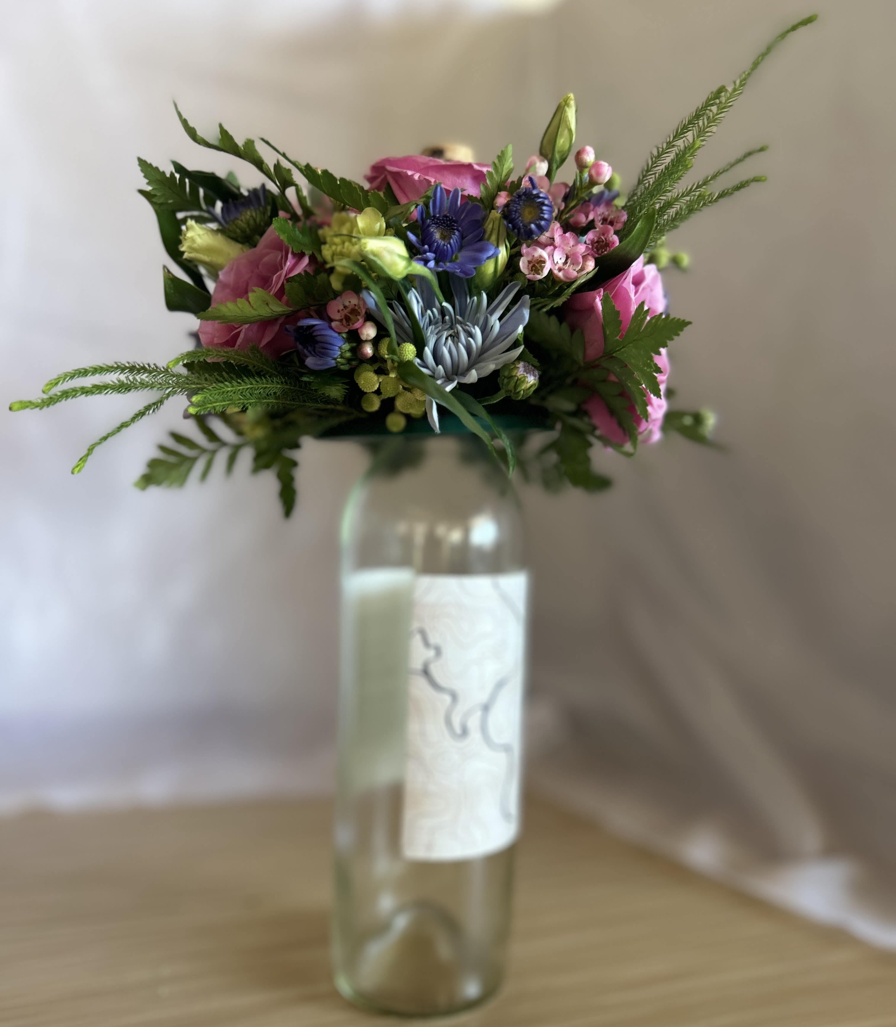 Colorful mixed bouquet with pink and blue flowers arranged in a tall glass bottle.