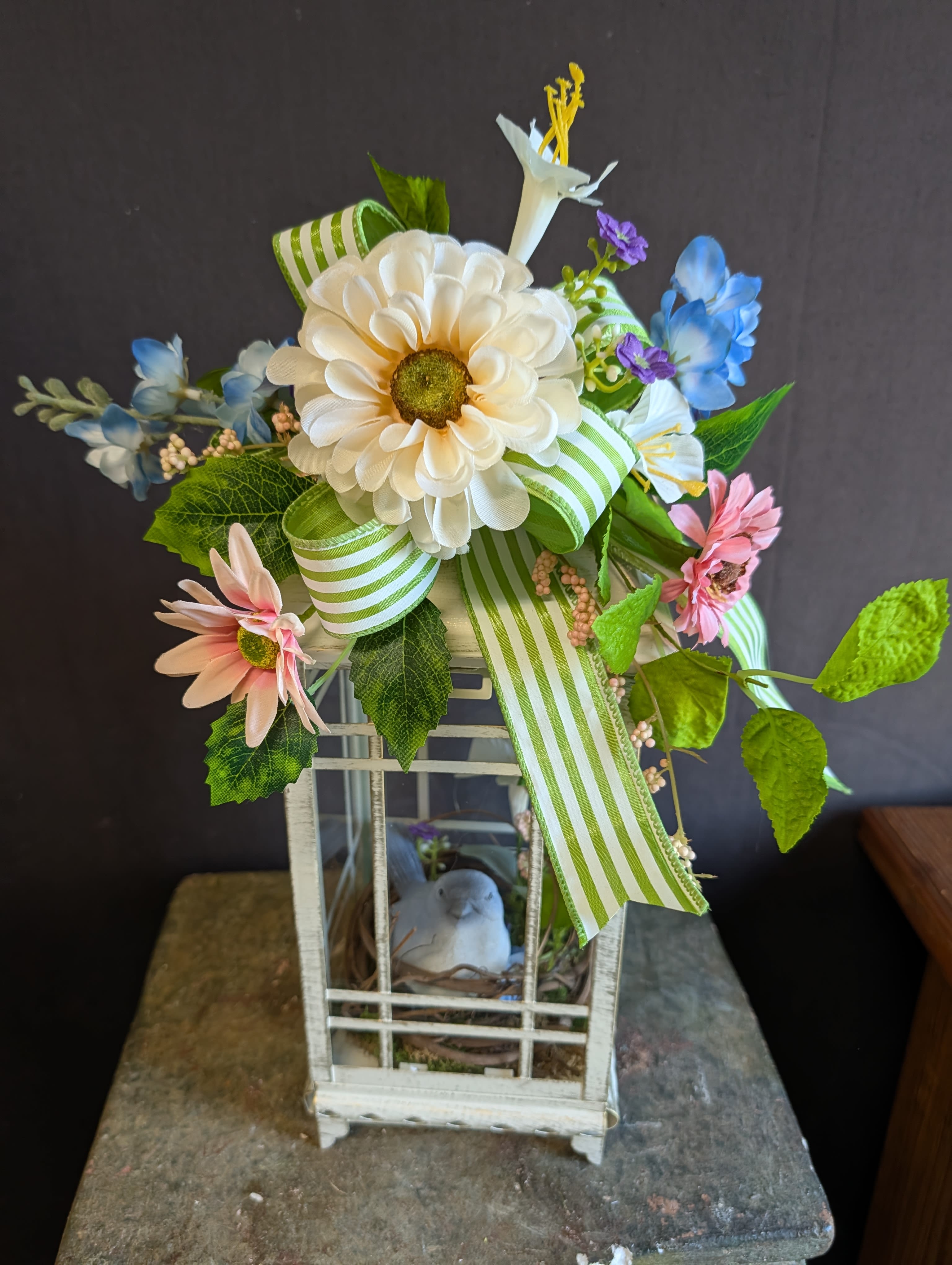 Garden Songbird Lantern				 - A charming rustic lantern featuring a delicate ceramic songbird nestled among moss and greenery. Topped with seasonal ribbon and silk foliage &amp; blooms, this piece brings a peaceful, cottage-inspired touch to indoor or covered outdoor décor. Perfect as a gift or accent for spring, Easter, or everyday elegance.	 		 				 				