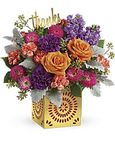 Bright mixed arrangement of orange roses, purple and pink flowers in a yellow cube vase with a gold “thanks” sign