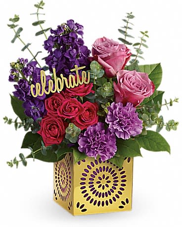 Bright arrangement of pink and red roses with purple flowers in a gold cube vase with a celebrate sign.