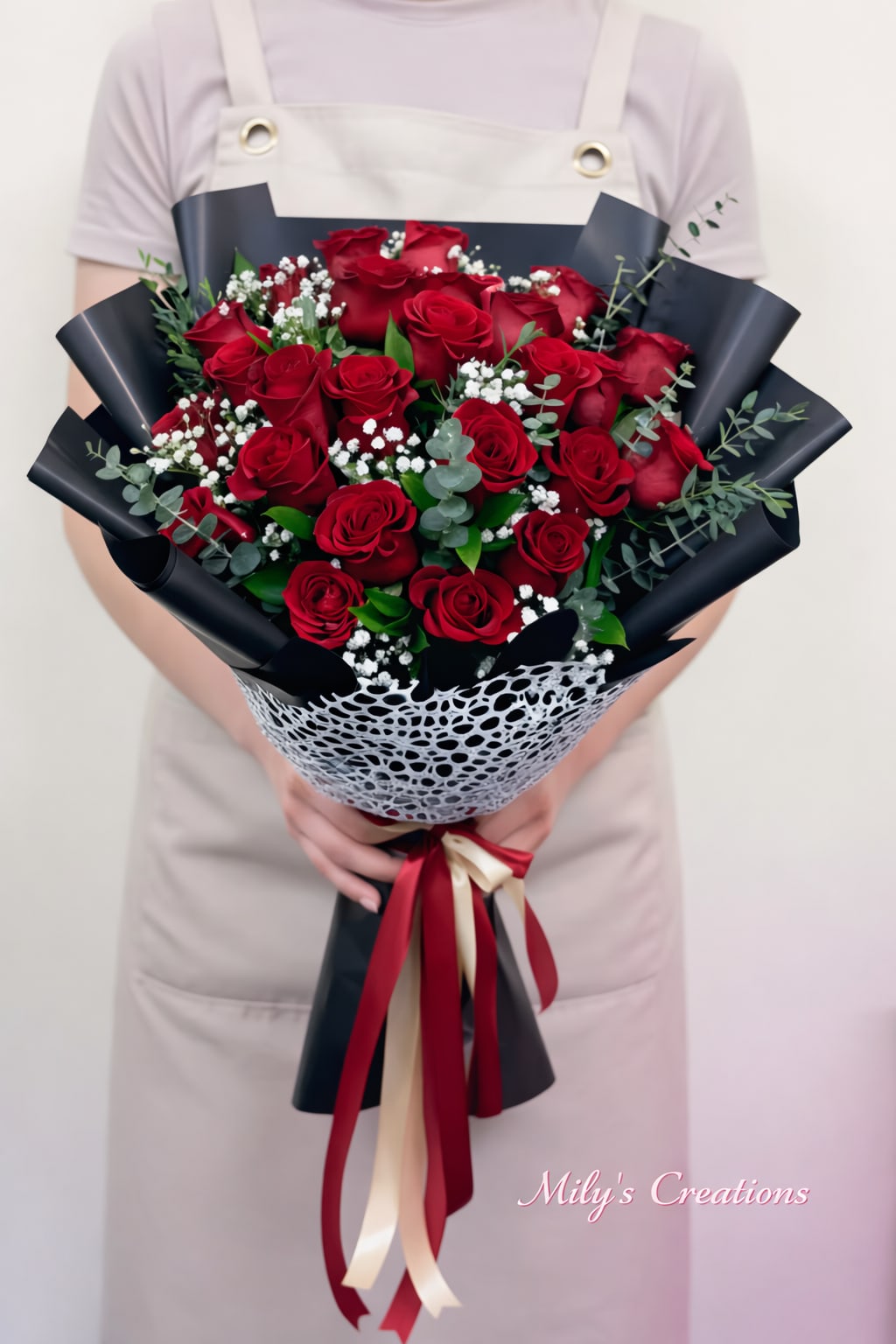 Handheld bouquet of red roses and white filler flowers wrapped in black paper with ribbons