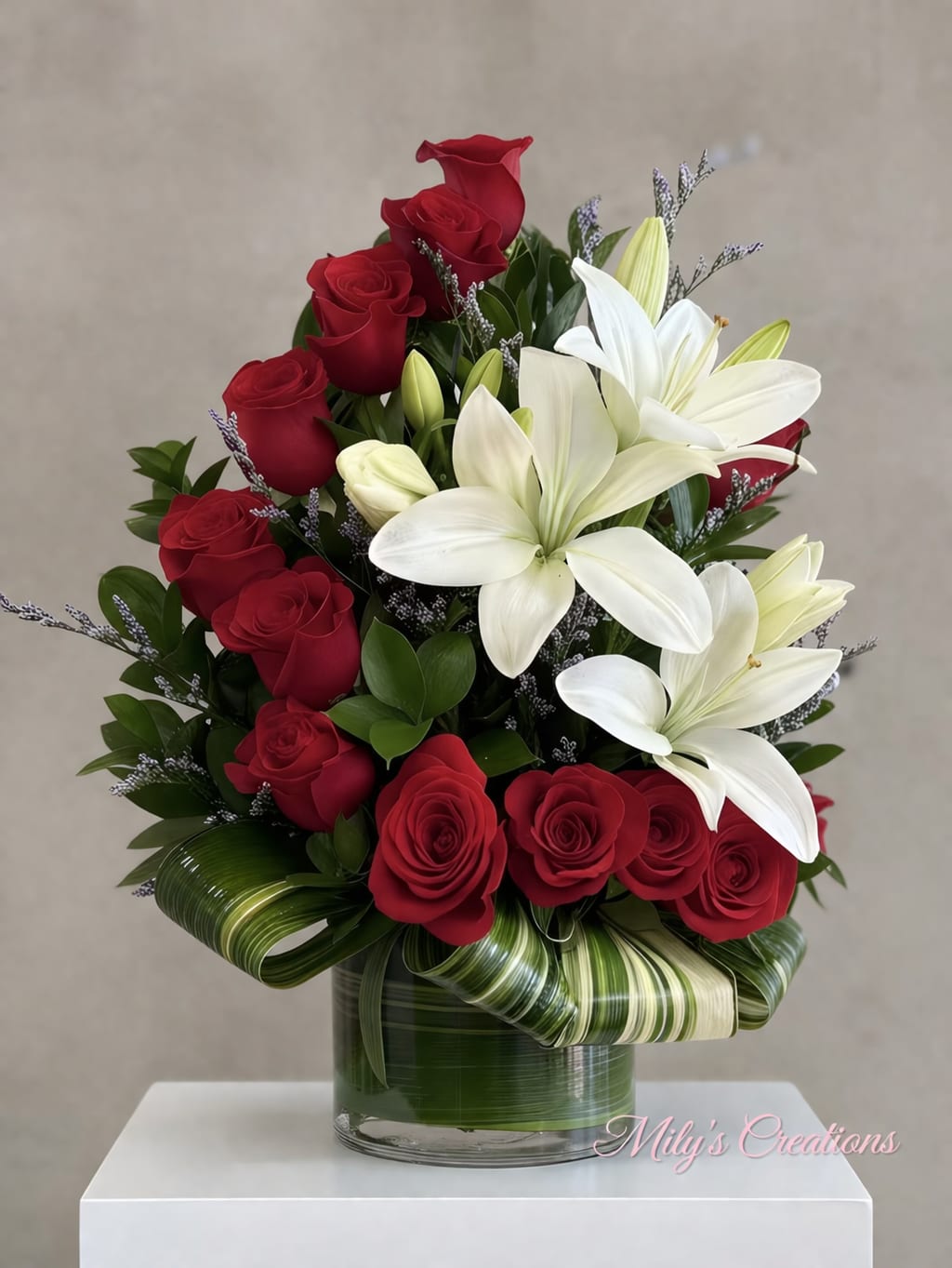Arrangement of red roses and white lilies in a clear vase with decorative green leaves.