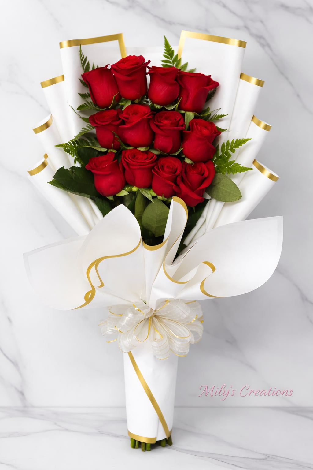 Hand-tied bouquet of red roses wrapped in white paper with gold trim and a decorative bow.