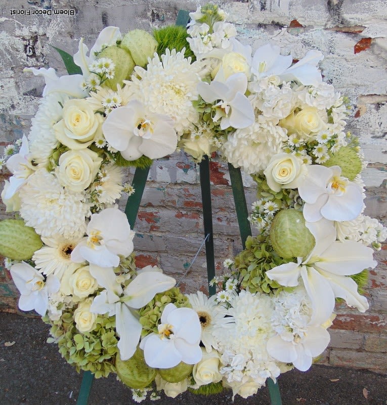 Standing wreath of white roses, orchids, lilies, and mums on a green easel.