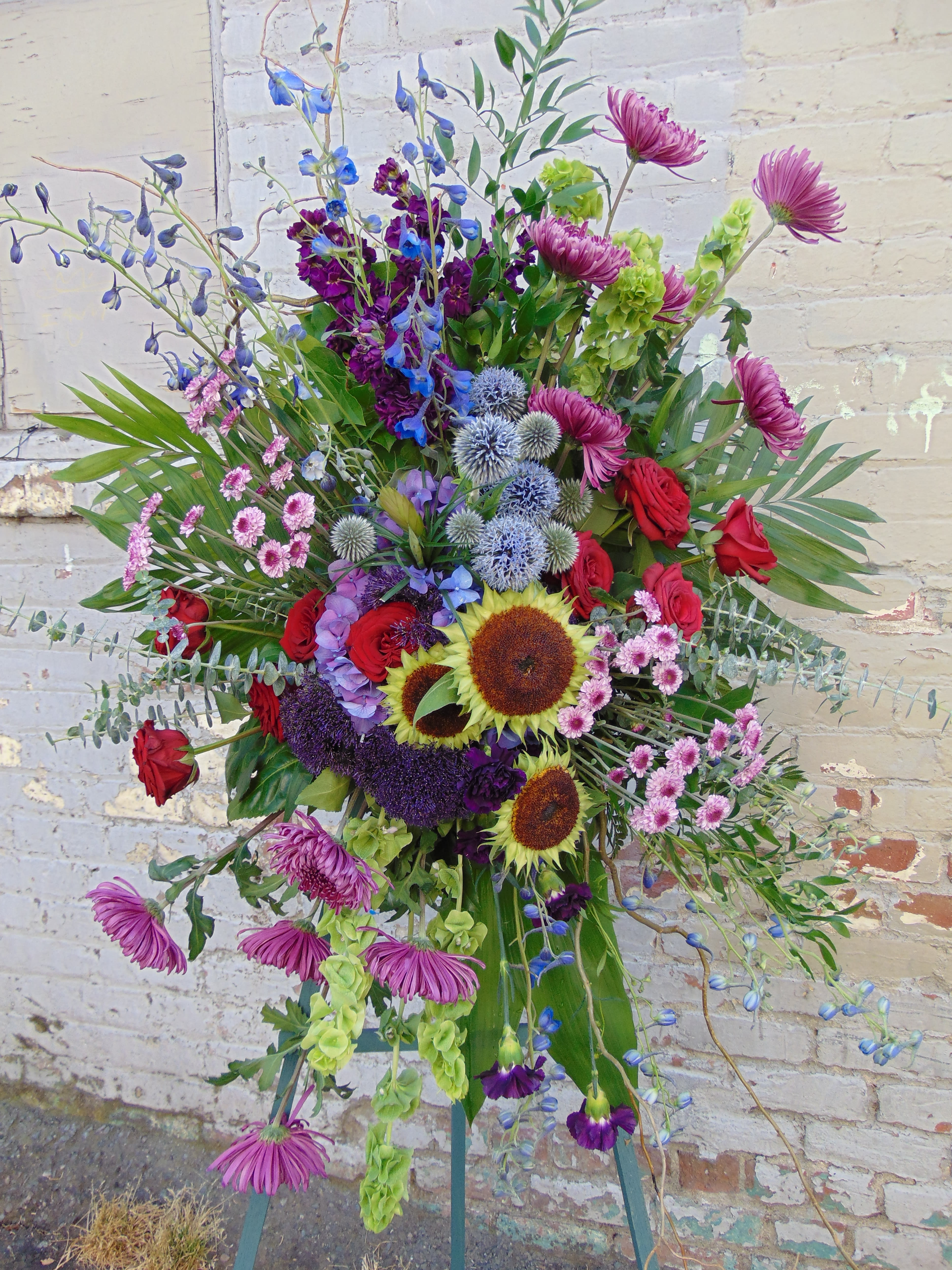 Designer's Choice Standing Spray - A standing spray made utilizing materials that are in season and is a custom design each time.  Photo is an example from our designers and can be used as size reference.  Specific color requests can be provided in your notes and our designers will do their utmost best to incorporate those requests. 