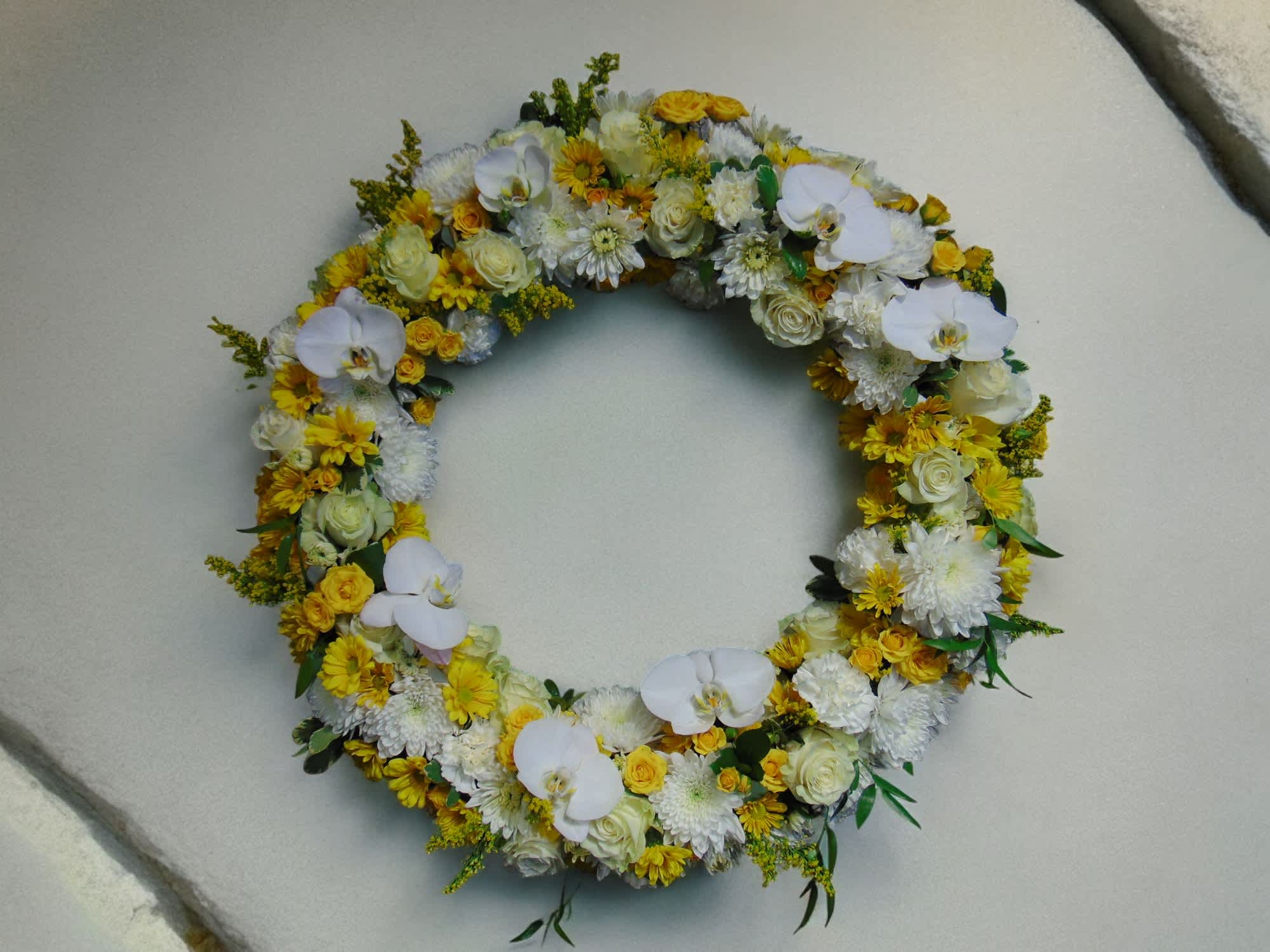 Large circular wreath of white orchids, roses, and yellow chrysanthemums arranged in a full ring