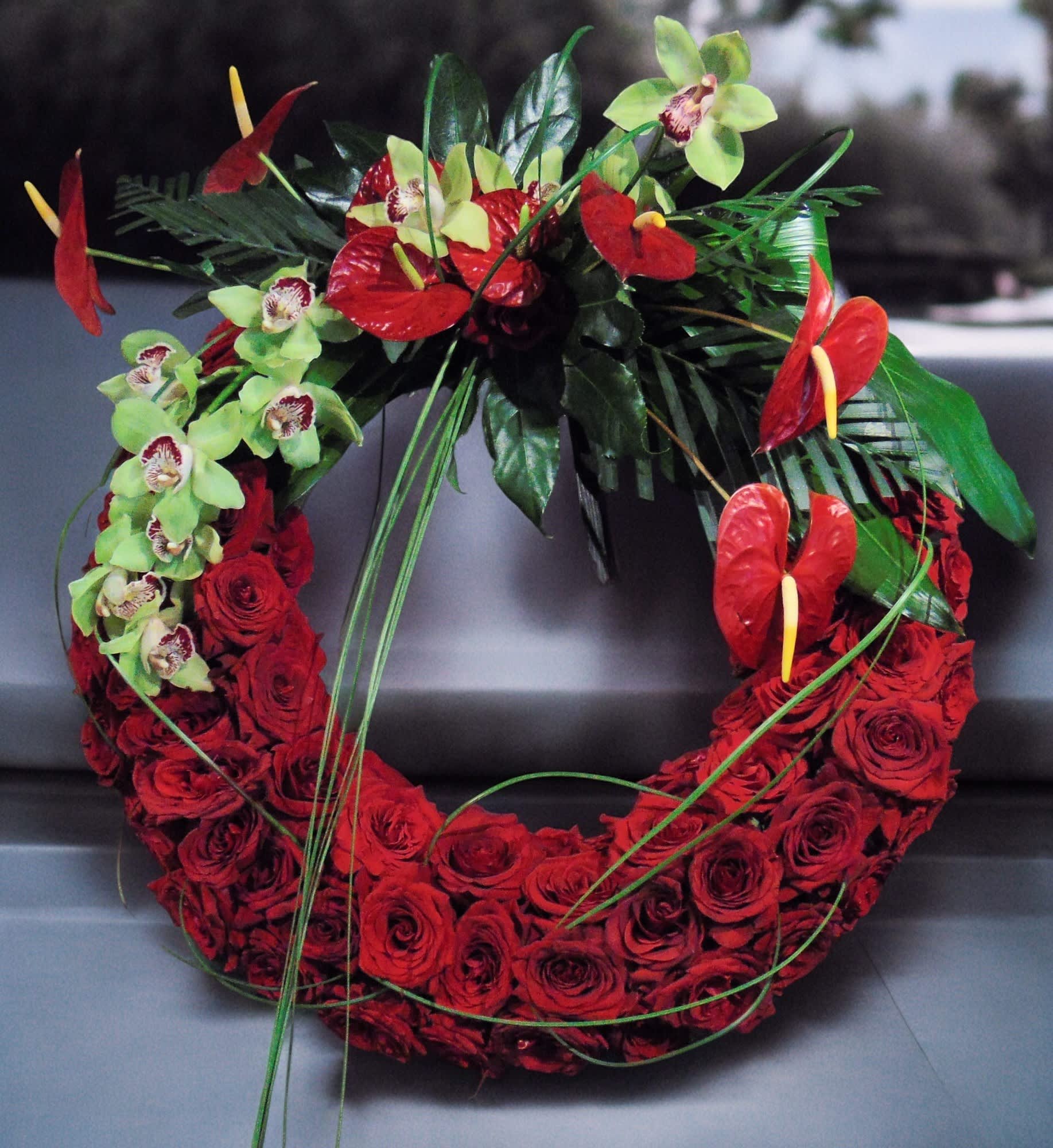 Circular wreath of red roses with green orchids and red tropical flowers on one side